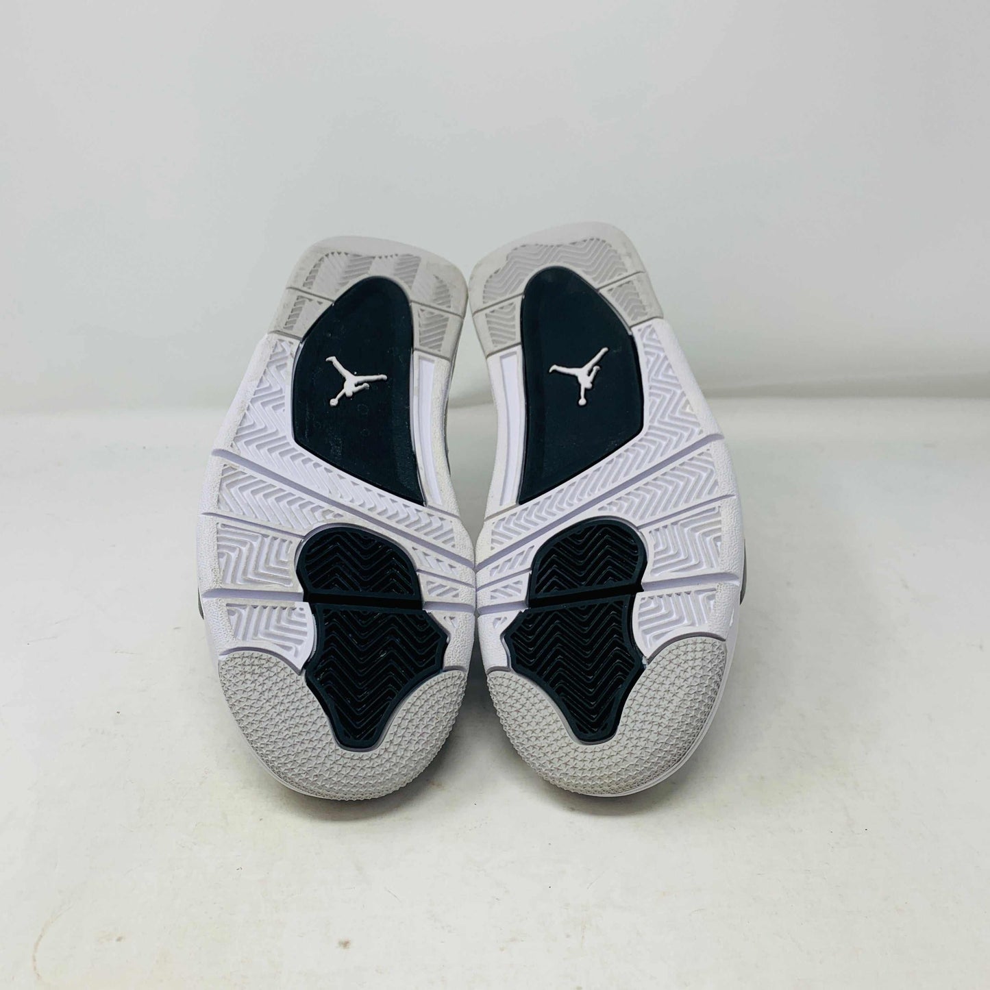 The Jordan 4 Military Black GS sneakers, featuring distinctive side netting and a logo on the tongue, are brand new and authentic in white and gray with black accents. They face forward on a white surface against a plain background, embodying modern style.