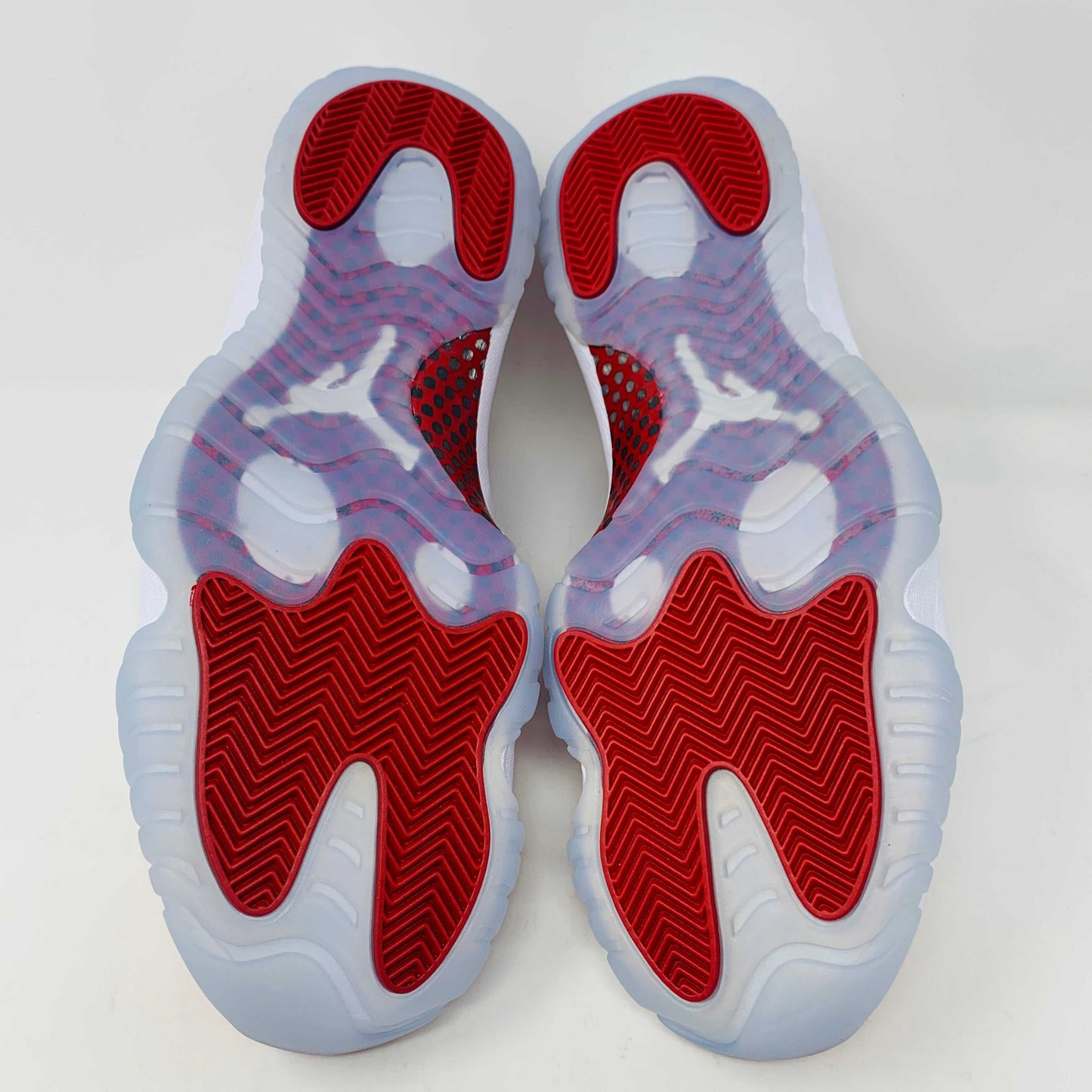 Jordan 11 Retro Cherry 2022 sneakers with red and white colorway, viewed from the bottom showing the red traction pattern.