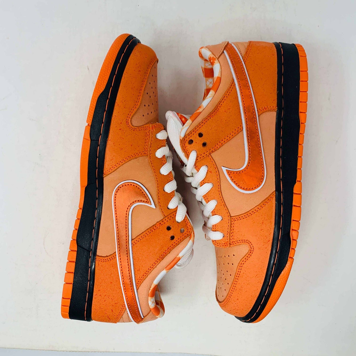 The authentic Nike SB Dunk Low Orange Lobster Concepts sneaker sits on a green and yellow Nike SB box. It features a white sole with black trim, an orange swoosh, and extra laces neatly positioned in front of the box.