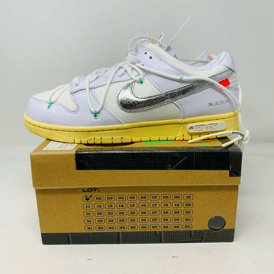 The Nike Dunk Low Off White Lot 1 sneaker, white with a metallic silver swoosh and vibrant accents, rests on a brown shoebox. Its unique lace design and 01 of 50 detailing highlight its 2021 release against a plain white backdrop.