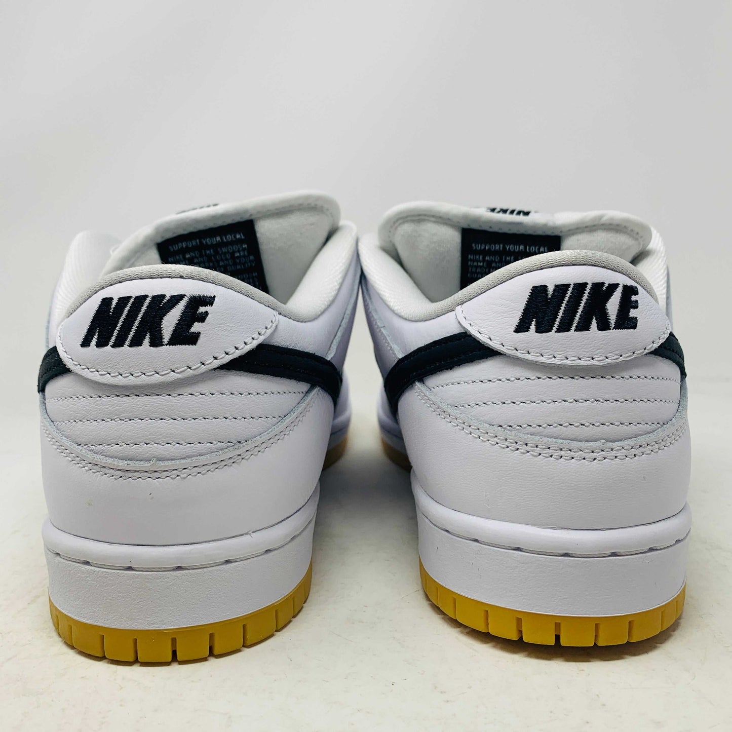 A brand new Nike SB Dunk Low in white with a black swoosh, white laces, and a gum sole rests on a 2023 purple Nike SB shoebox featuring bold white text. The profile view showcases its authentic design.
