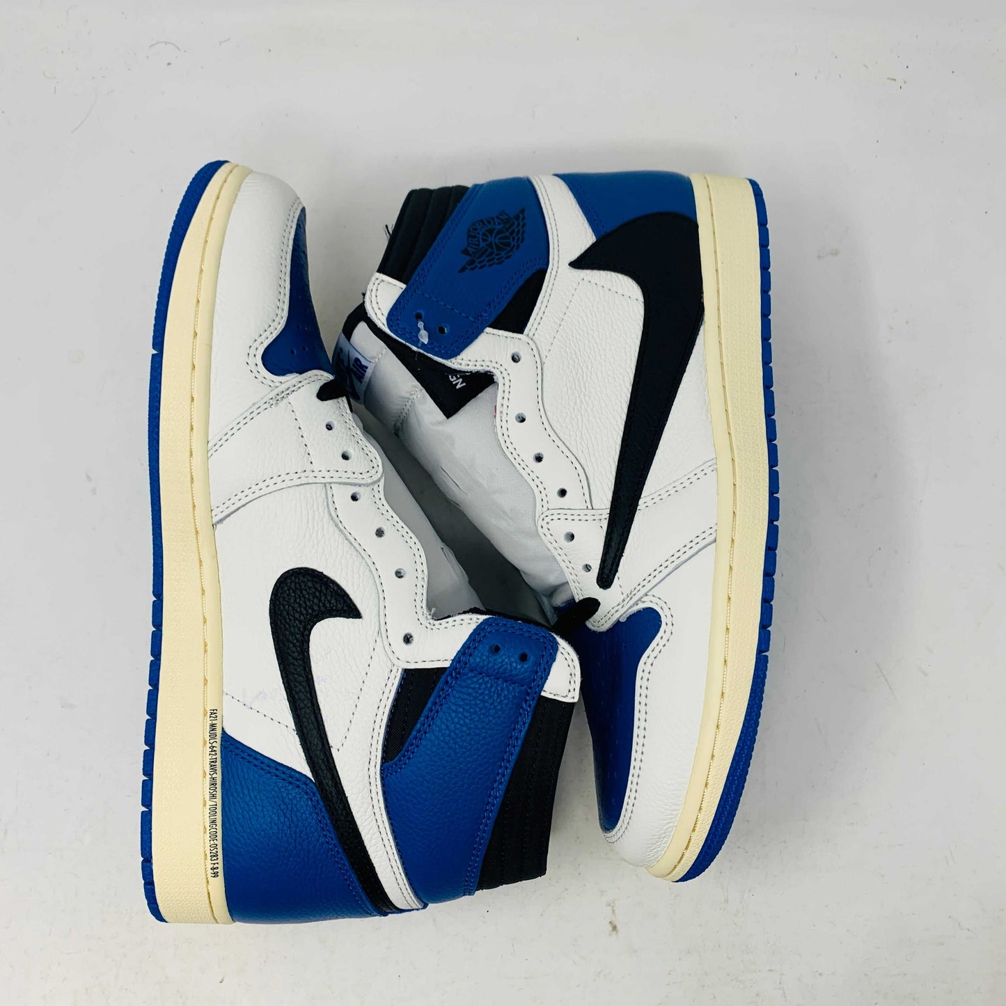 The Jordan 1 Retro High OG SP Fragment x Travis Scott is a new high-top sneaker featuring a blue, white, and black design with a unique backward Nike swoosh. It comes in a transparent, branded box adorned with butterfly and text details, boasting a thick sole and classic 1985 Air Jordan design.