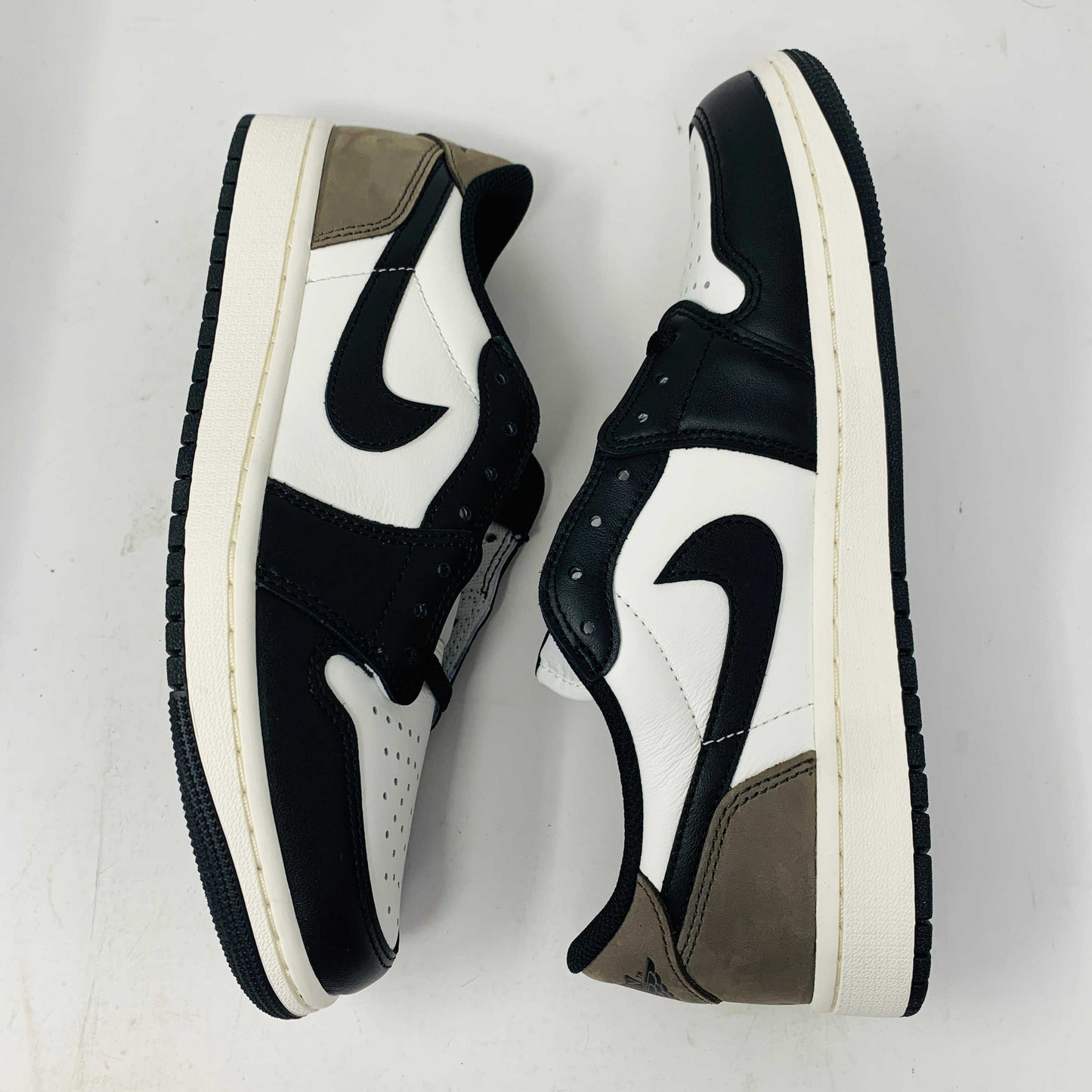 The Jordan 1 Retro Low OG Mocha sneakers, featuring a black swoosh logo on white uppers with black and brown accents, have sleek black laces and soles. They align with the 2024 style trend and are showcased against a white background. Box condition is good.