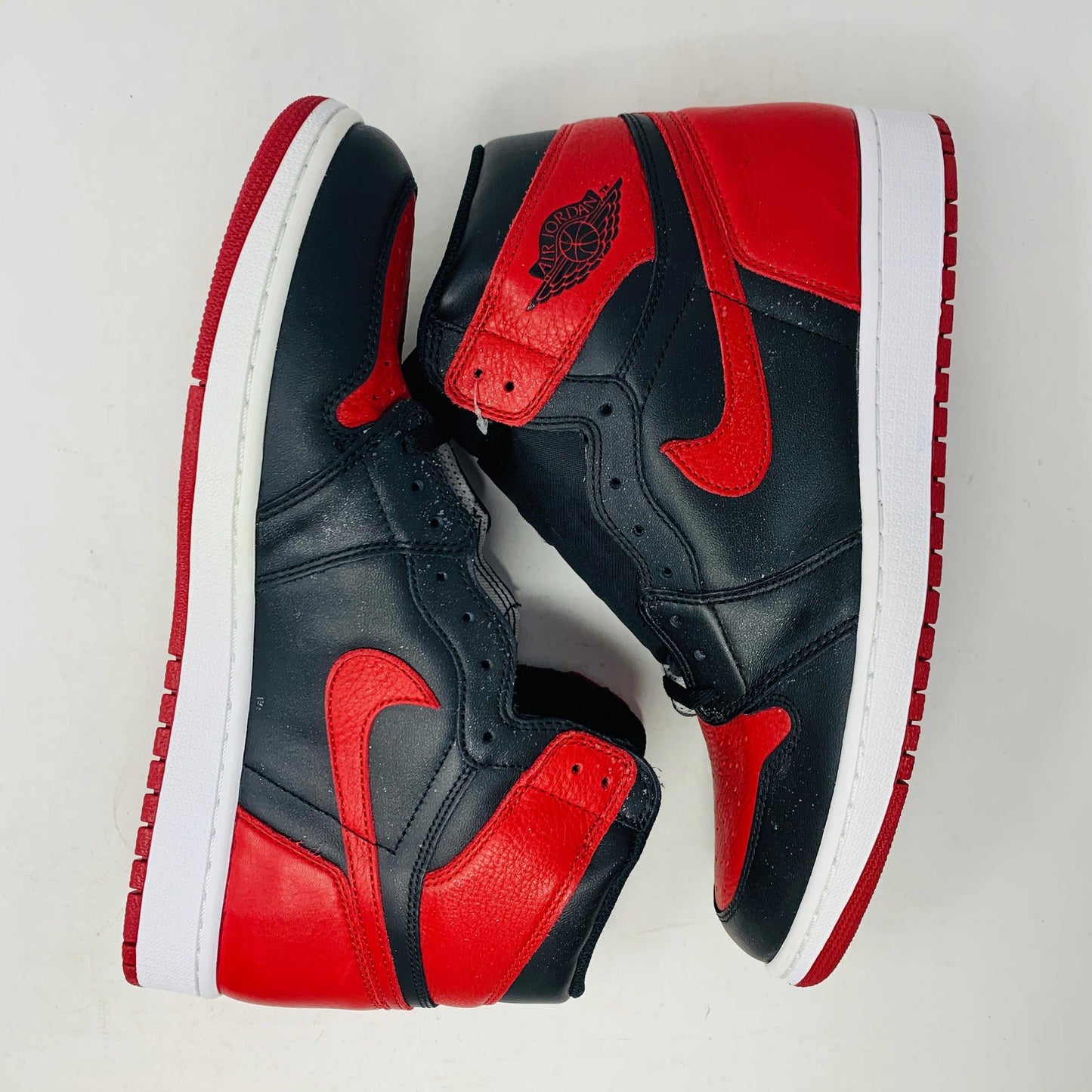 The Jordan 1 High Bred 2016 sneakers, by Jordan, are brand-new black and red high-tops with a white sole. Viewed from above, they showcase an unlaced look with a perforated design on the toe area.