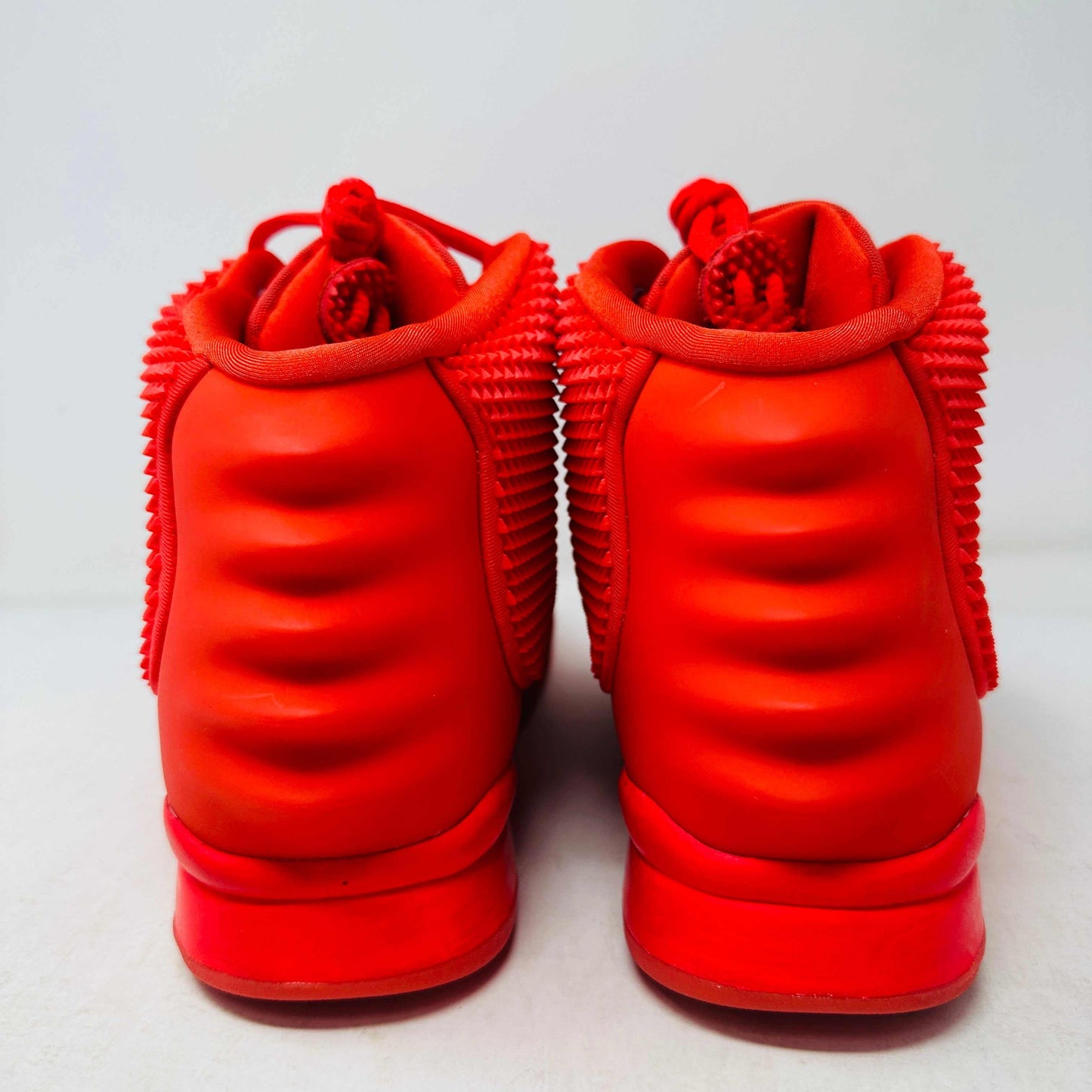 A pair of Nike Air Yeezy 2 Red October high-top sneakers, 100% authentic and brand new, features laces, a midfoot strap, and textured side detailing. Seen from the front against a white background, these bright red shoes showcase their unique style.