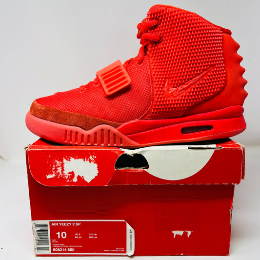 The Nike Air Yeezy 2 Red October, a vivid red high-top sneaker, features a textured upper, prominent midfoot strap, and clear branding. Displayed on its shoebox with size 10 marked, it shows light wear reminiscent of 2014 style.