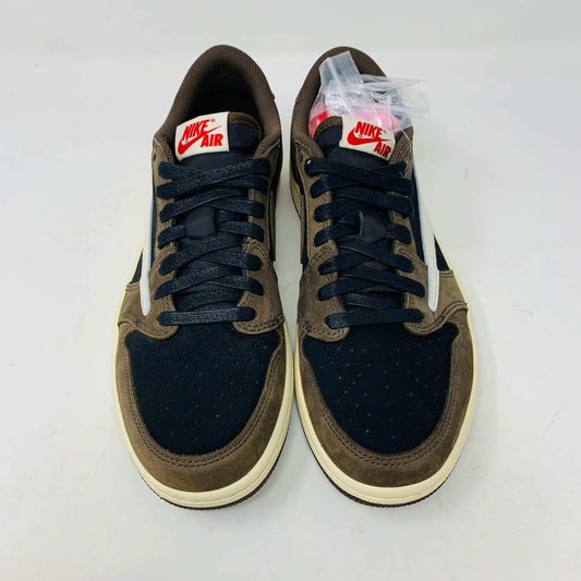 A pair of BRAND NEW Jordan 1 Low OG Travis Scott Mocha sneakers in black and brown, featuring a white swoosh, displayed on a brown shoe box with a red logo. 100% Authentic with EXTRA LACES partially visible inside.