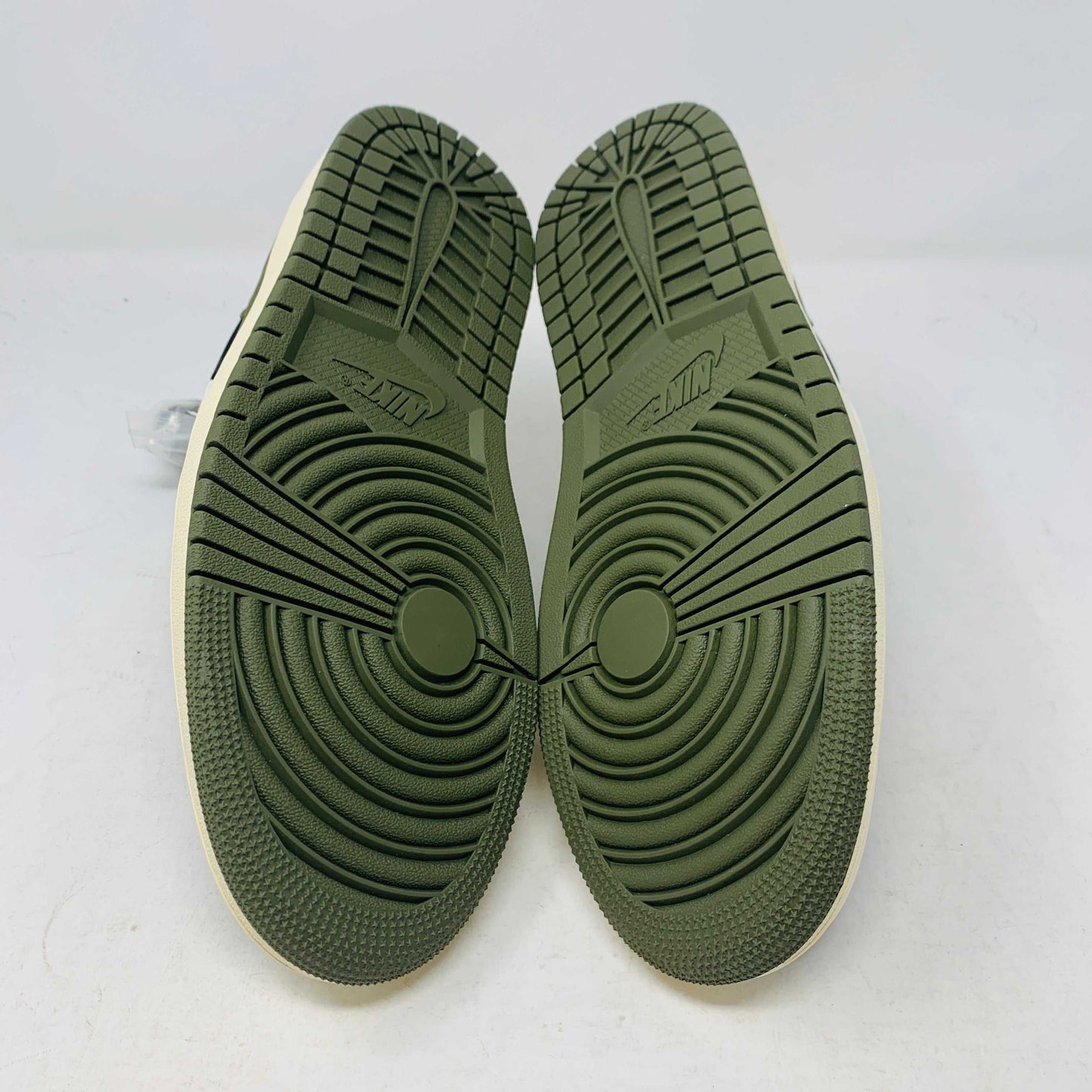A black, white, and olive green Jordan 1 Retro Low OG SP Travis Scott Olive (W) sneaker from Nike is displayed on a matching box. This brand new shoe sports a large reversed swoosh and cream-colored sole. The box showcases the green Nike logo with 1985 Air Jordan 1 text for these authentic 2023 shoes.