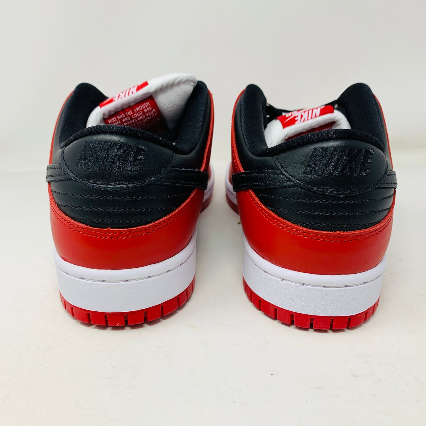 A brand new Nike SB Dunk Low J-Pack Chicago sneaker in red, white, and black sits on a purple Nike SB box with extra white laces, highlighted by a black swoosh and guaranteed 100% authentic.