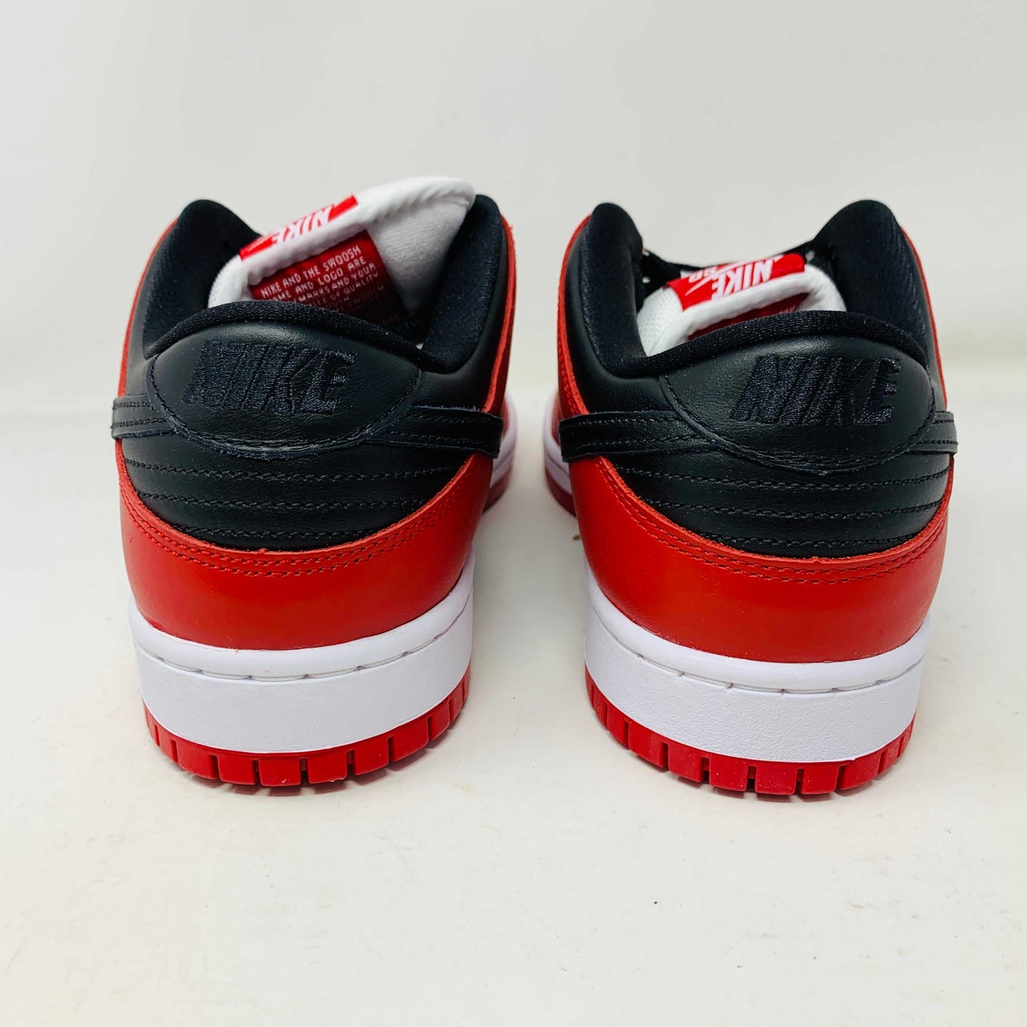 A brand new Nike SB Dunk Low J-Pack Chicago sneaker in red, white, and black sits on a purple Nike SB box with extra white laces, highlighted by a black swoosh and guaranteed 100% authentic.