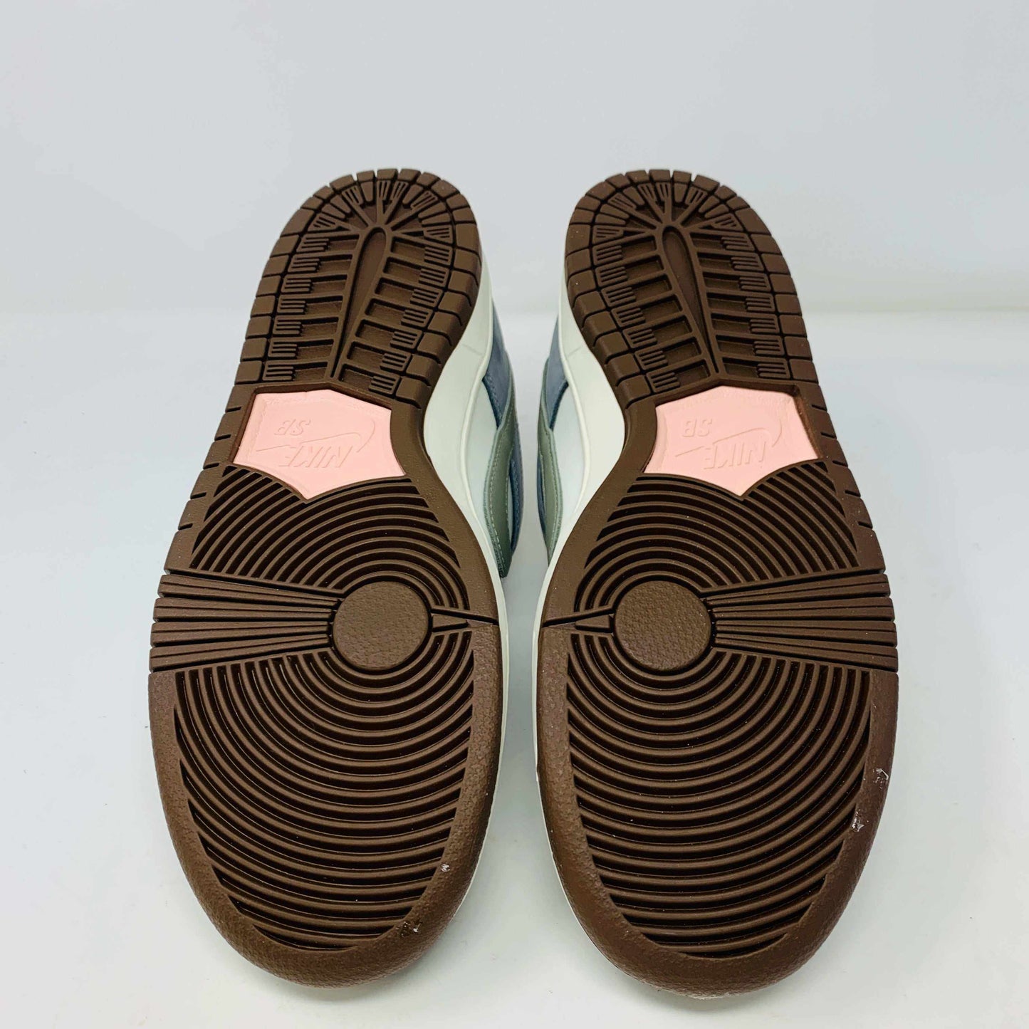 The Nike SB Dunk Low Yuto Horigome sneaker, with a white and light blue design featuring a gray swoosh, is displayed on a white Nike SB box. The authentic shoe has pink and brown laces, a brown sole, and an embroidered logo on the heel.