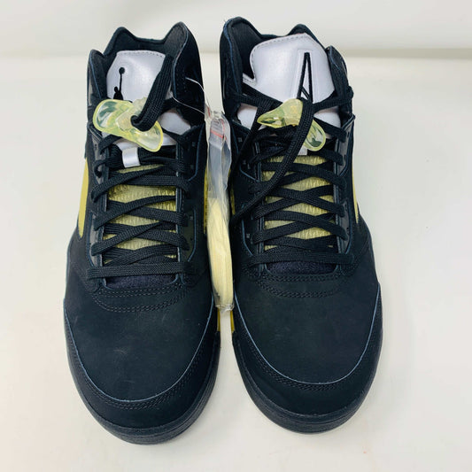 The black and yellow Jordan 5 Retro A Ma Maniére Dusk high-top sneakers, featuring black laces and a white tongue, are displayed side by side on a plain white background.