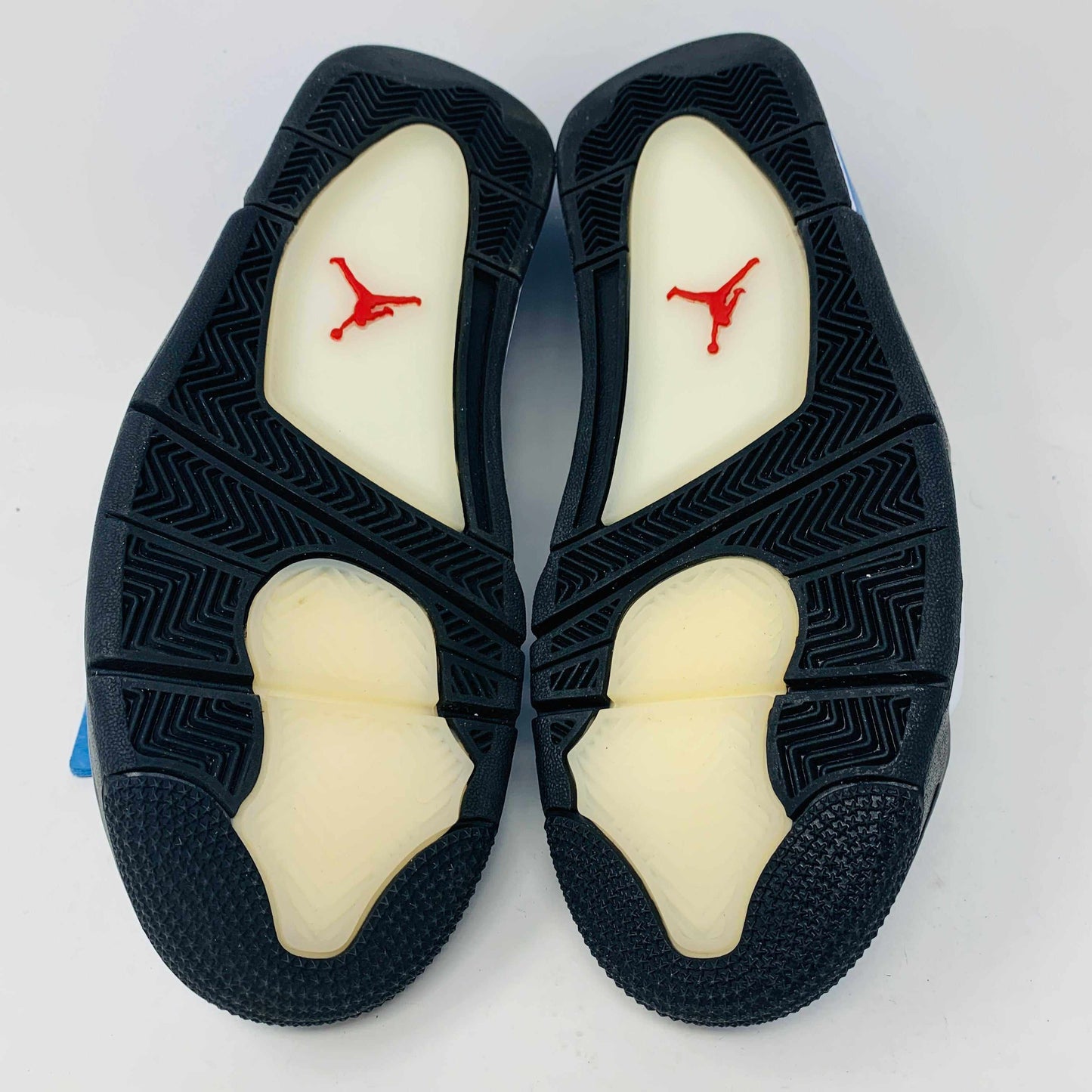 The Jordan 4 Retro Travis Scott Cactus Jack sneaker in blue, accented with black and red, features a visible air unit in the heel and a Jumpman logo hang tag, packaged in a black speckled box with an orange Jumpman logo and AIR.