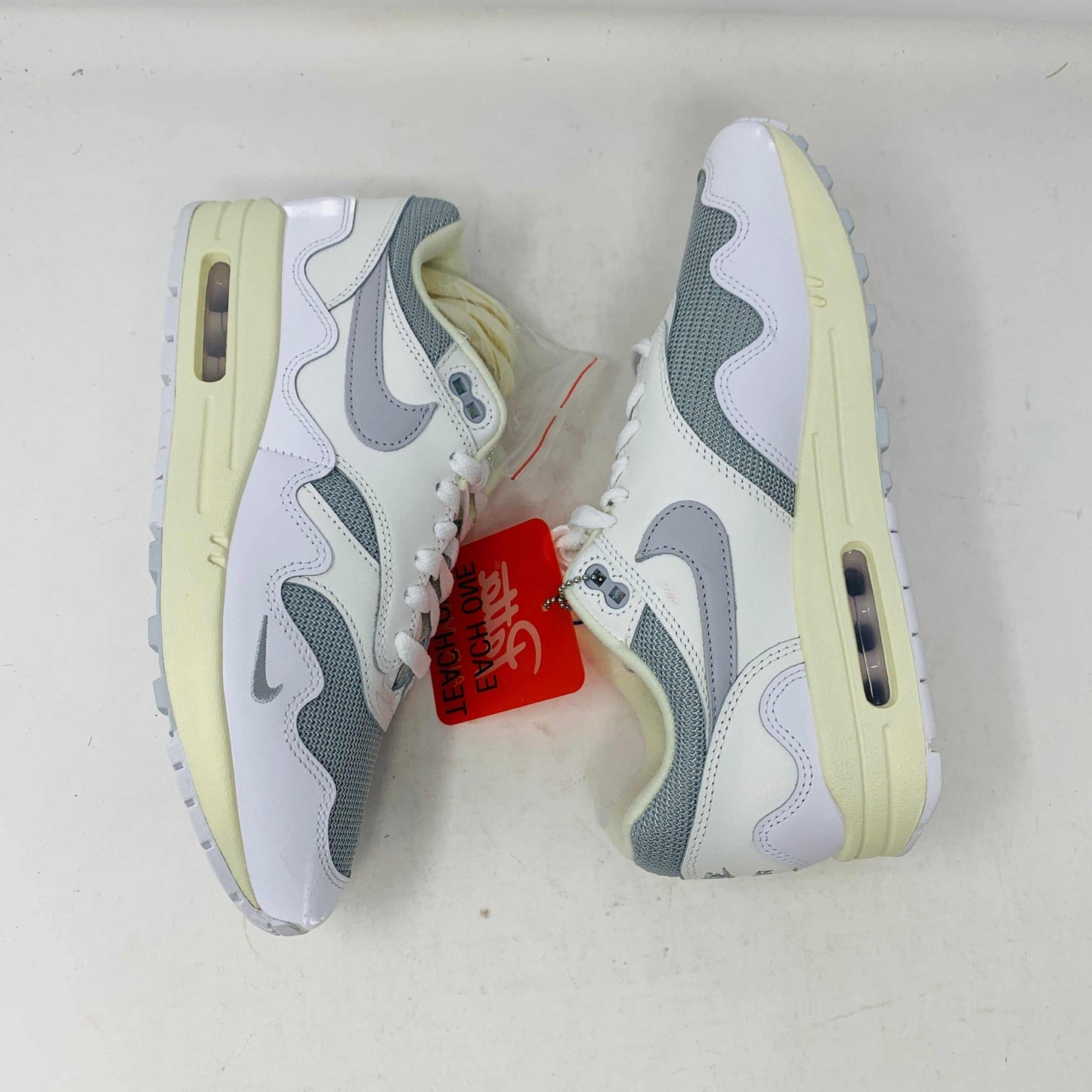 The Nike Air Max 1 Patta Waves White, a brand new sneaker, features a visible air cushion sole and swoosh logo. It comes elegantly displayed on a matching P.G.L.F.A. box with extra laces in a plastic bag attached to the tongue.