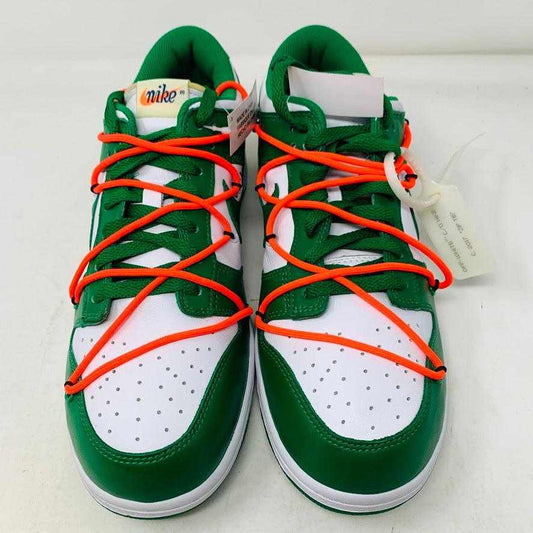 The Nike Dunk Low Off White Pine Green sneaker, accented with bright orange laces, rests on a shiny silver box. This authentic 2019 release by Nike boasts a sleek white tag, highlighting its new allure.