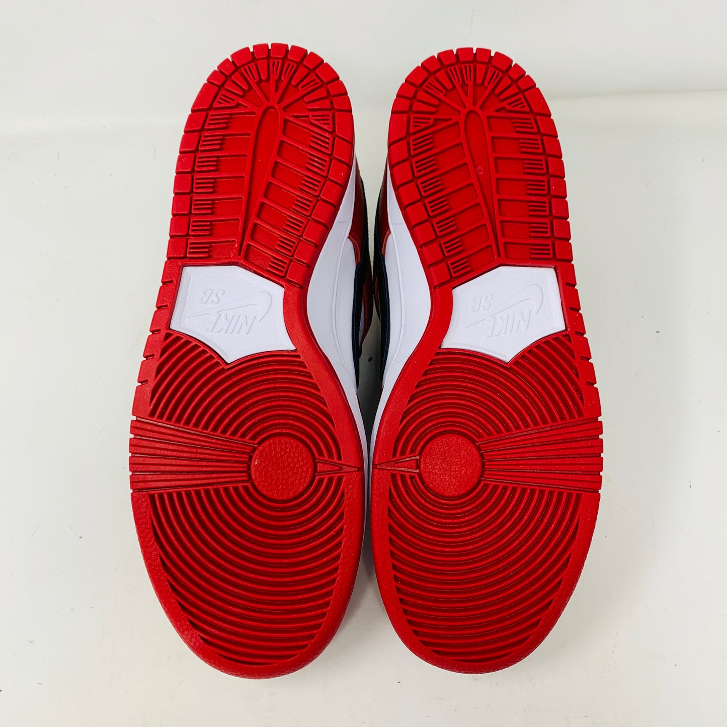 A brand new Nike SB Dunk Low J-Pack Chicago sneaker in red, white, and black sits on a purple Nike SB box with extra white laces, highlighted by a black swoosh and guaranteed 100% authentic.