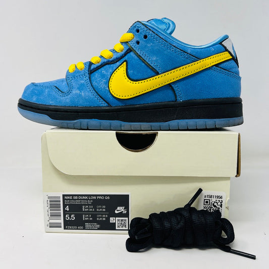 A Nike SB Dunk Low The Powerpuff Girls Bubbles sneaker, with blue uppers and a yellow swoosh, is showcased on its box. It has blue laces, a dark sole, and includes extra black laces. This 2023 Nike design is both stylish and versatile.