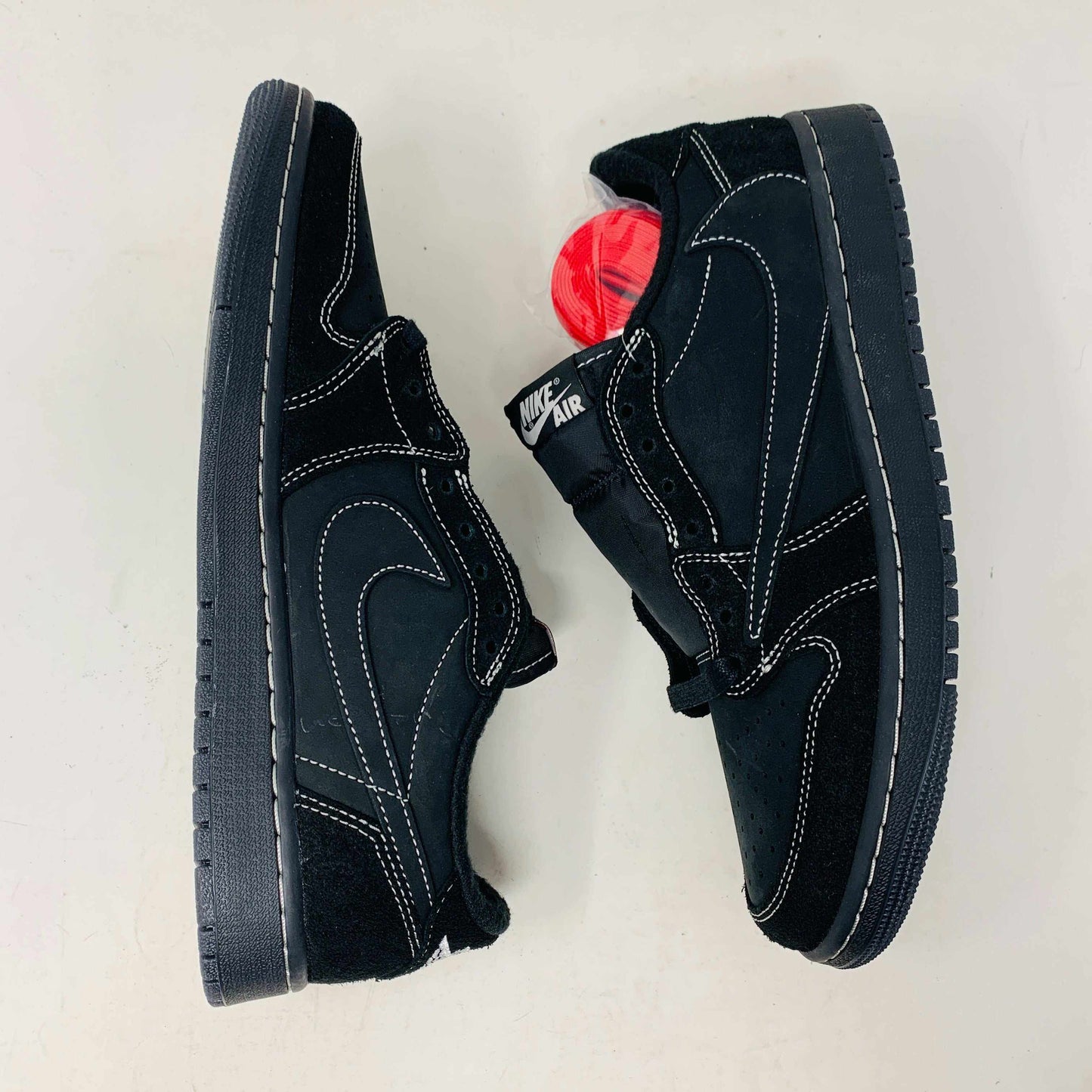 The Jordan 1 Low Travis Phantom sneakers, in black with white stitching, rest on a matching box. Authenticity shines through their design, enhanced by red inserts and the boxs subtle features.