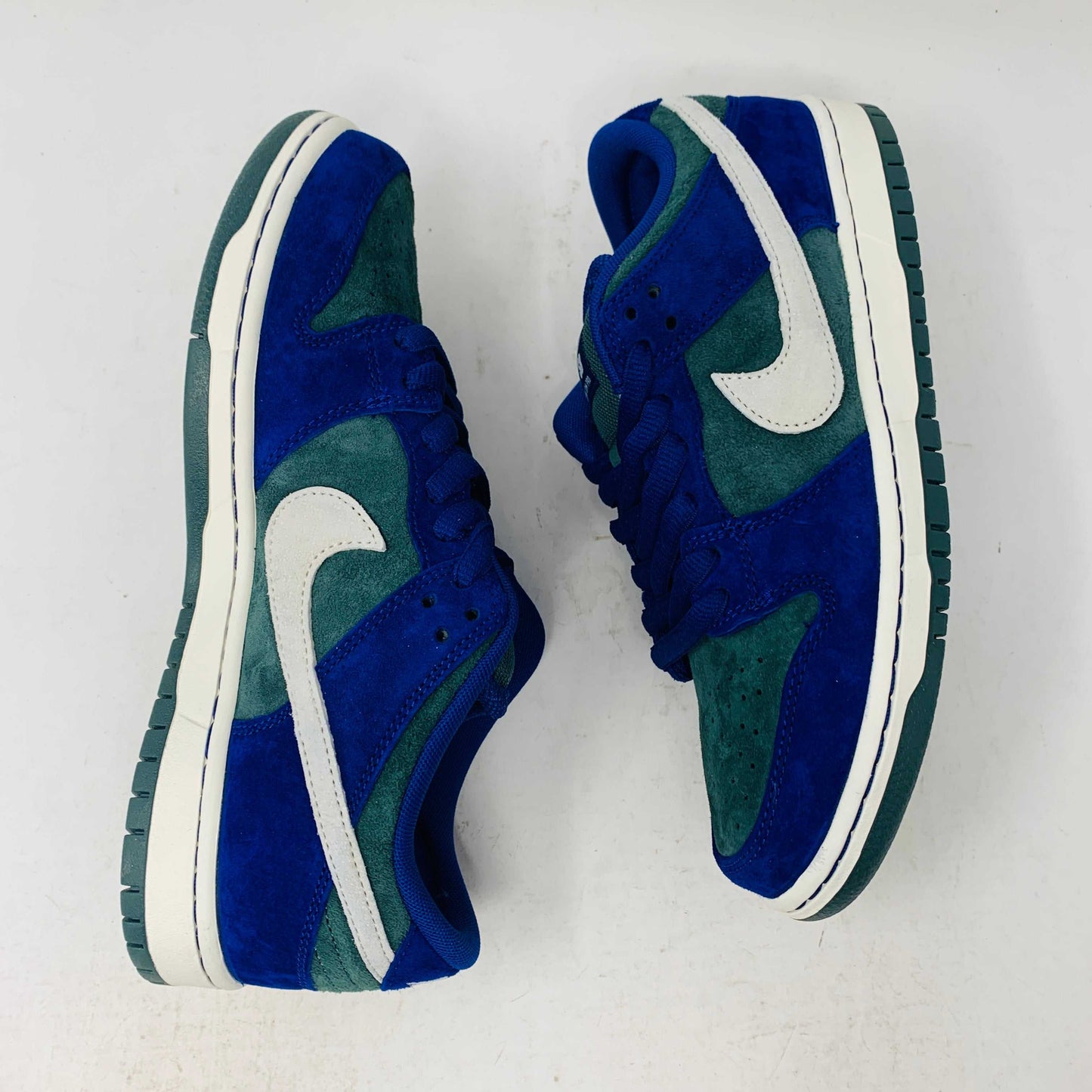 The Nike SB Dunk Low Deep Royal Blue sneaker, featuring a sleek blue and green design with a white swoosh, sits atop a purple Nike box. A bonus set of green laces accompanies the shoe, perfect for updating your style in 2024.