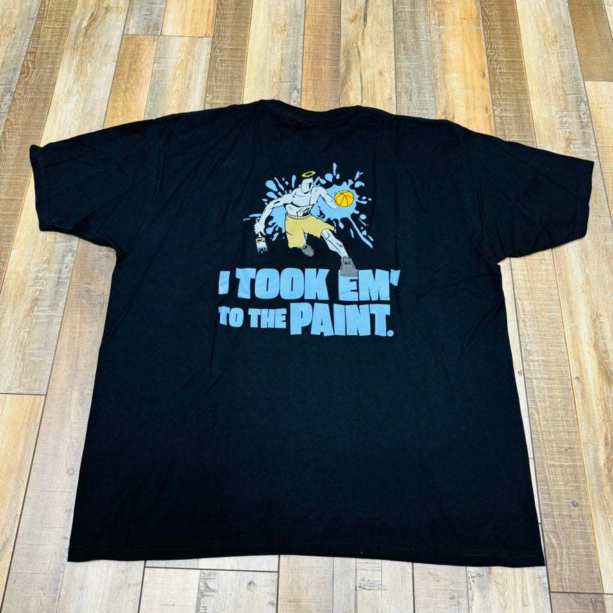 Holy Ground HG And-1 Tee in black, featuring a small white chest logo, is laid flat on a wooden floor.