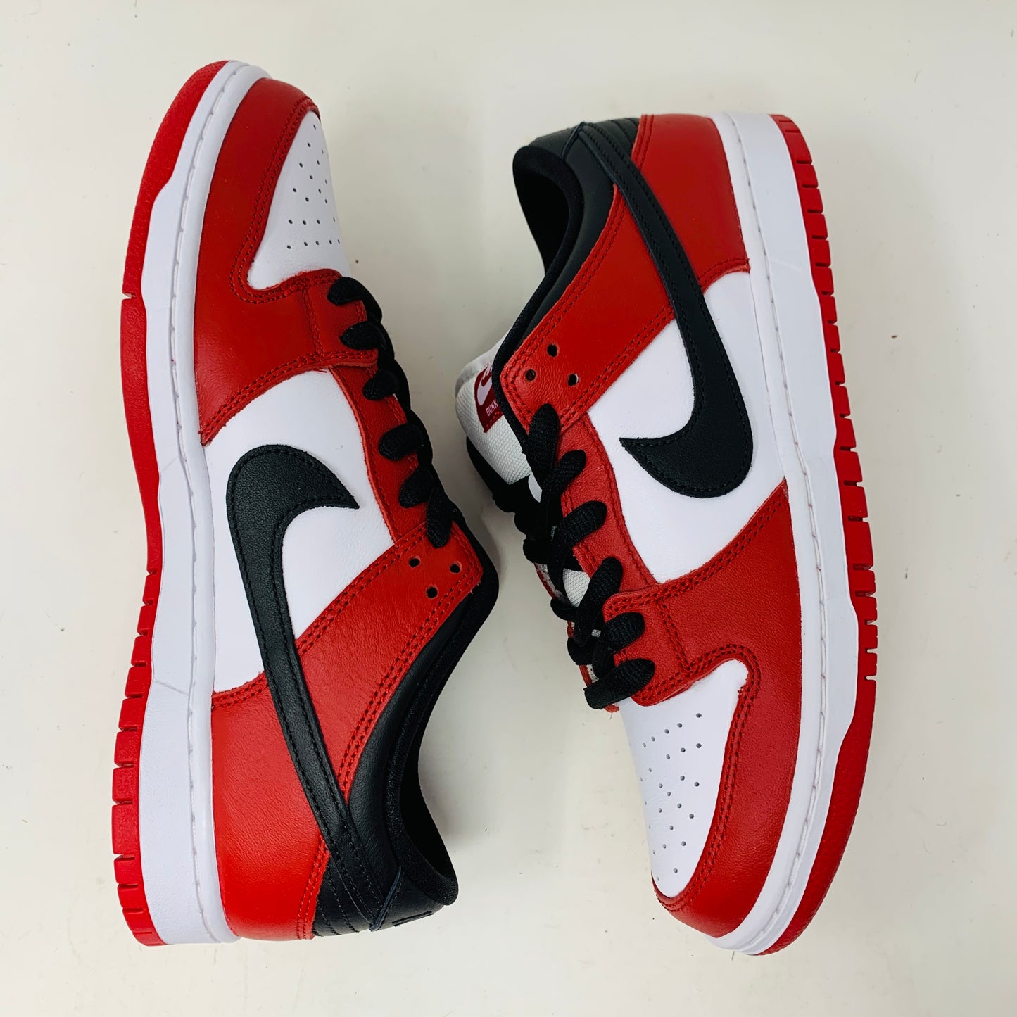 A brand new Nike SB Dunk Low J-Pack Chicago sneaker in red, white, and black sits on a purple Nike SB box with extra white laces, highlighted by a black swoosh and guaranteed 100% authentic.