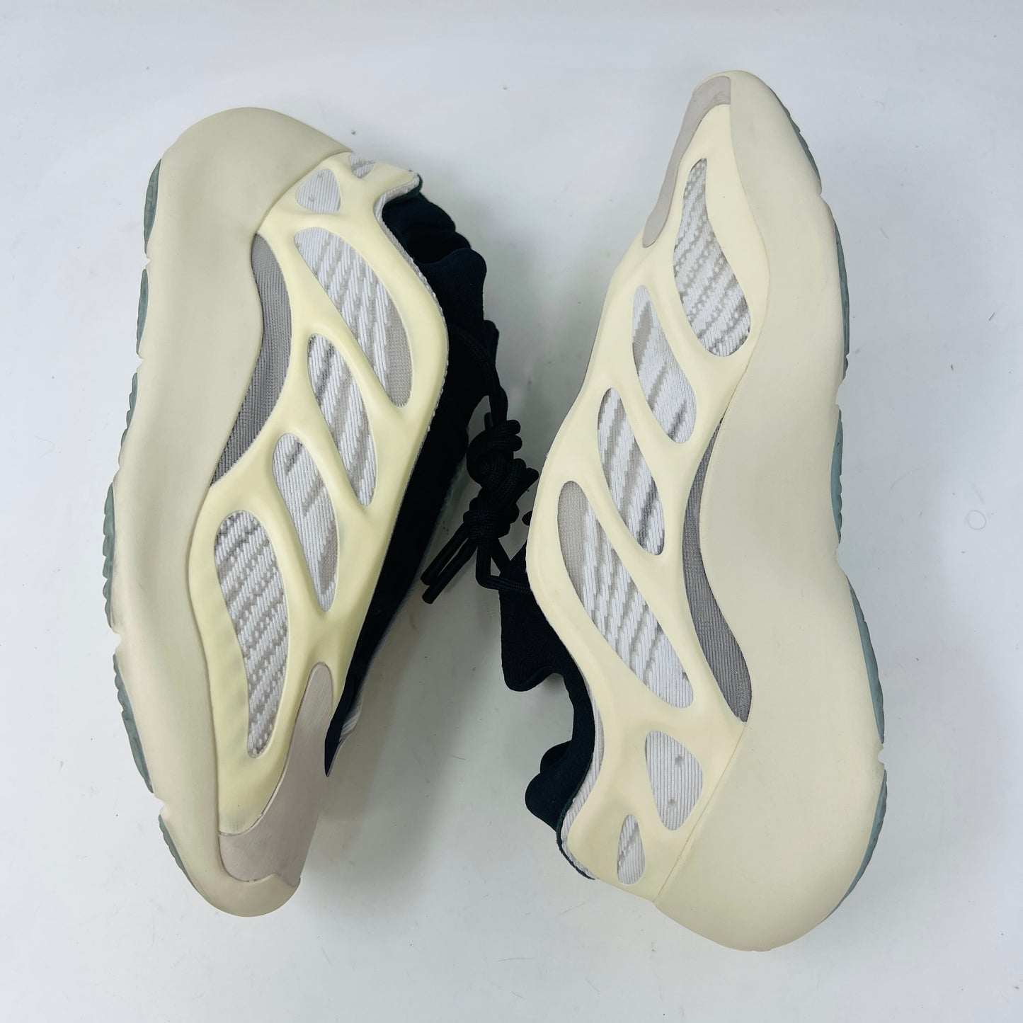 The adidas Yeezy 700 V3 Azael features a futuristic design with a black mesh upper, white and beige sculpted overlays, and an intricate lacing system. It has a sleek, modern look set against a plain white background, showing minimal wear for that fresh out-of-the-box condition.