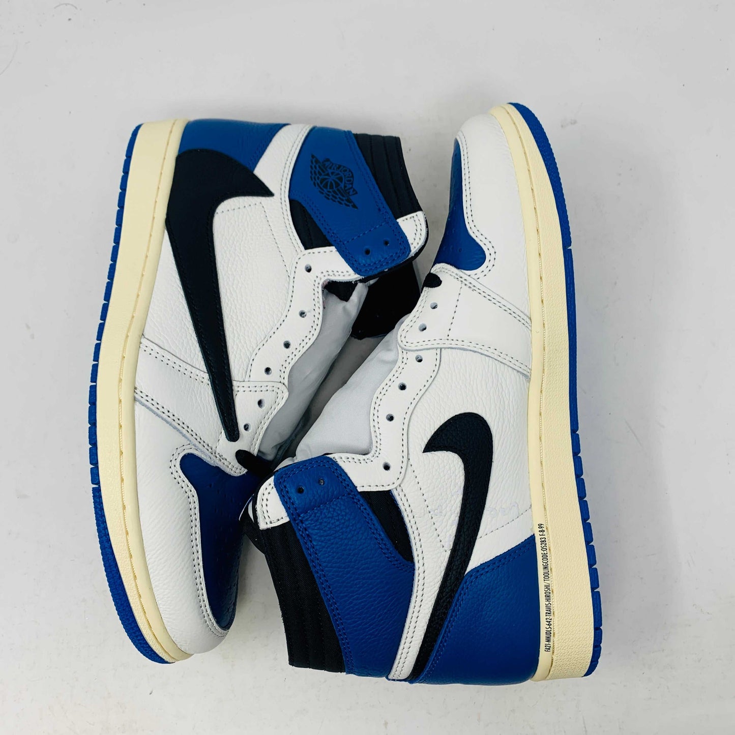 The Jordan 1 Retro High OG SP Fragment x Travis Scott is a new high-top sneaker featuring a blue, white, and black design with a unique backward Nike swoosh. It comes in a transparent, branded box adorned with butterfly and text details, boasting a thick sole and classic 1985 Air Jordan design.