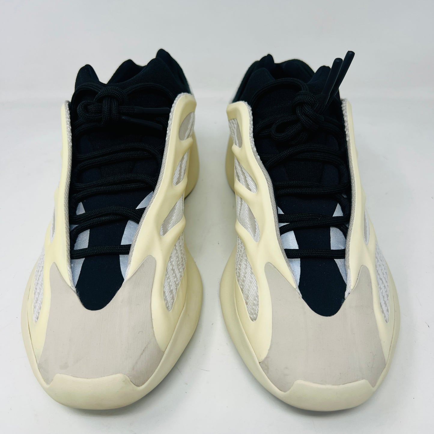 The adidas Yeezy 700 V3 Azael features a futuristic design with a black mesh upper, white and beige sculpted overlays, and an intricate lacing system. It has a sleek, modern look set against a plain white background, showing minimal wear for that fresh out-of-the-box condition.