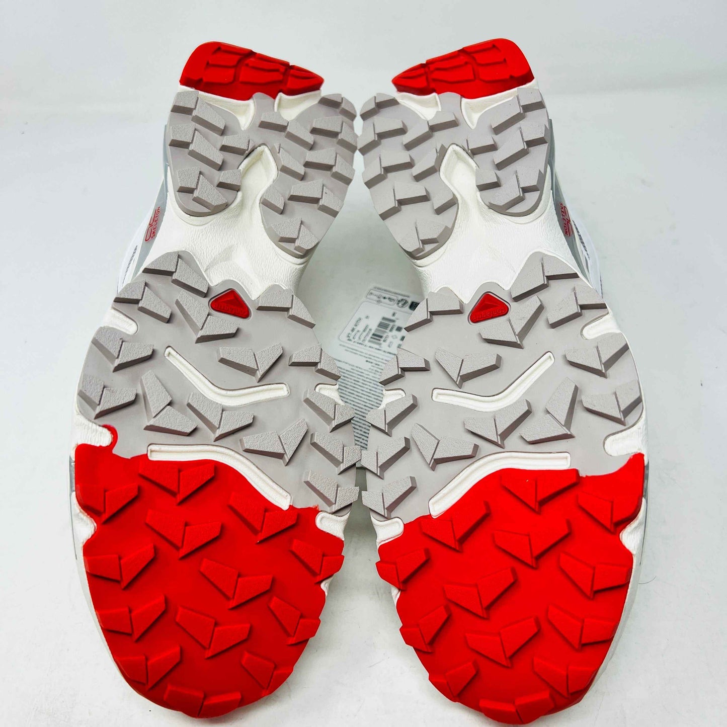The Salomon XT-4K Kith Kithmas White Red sneakers rest on a black Kith box, with an extra laces bag. The shoes are 100% authentic, showcasing red accents and branding details.