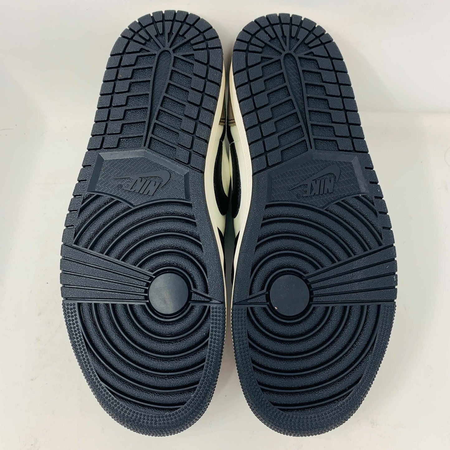 The image shows the soles of brand new Jordan 1 Retro Low OG Mocha shoes with a Nike logo. These black soles have intricate tread patterns featuring circular designs at the forefoot and linear grooves along the length for traction, exemplifying their 2024 design excellence.