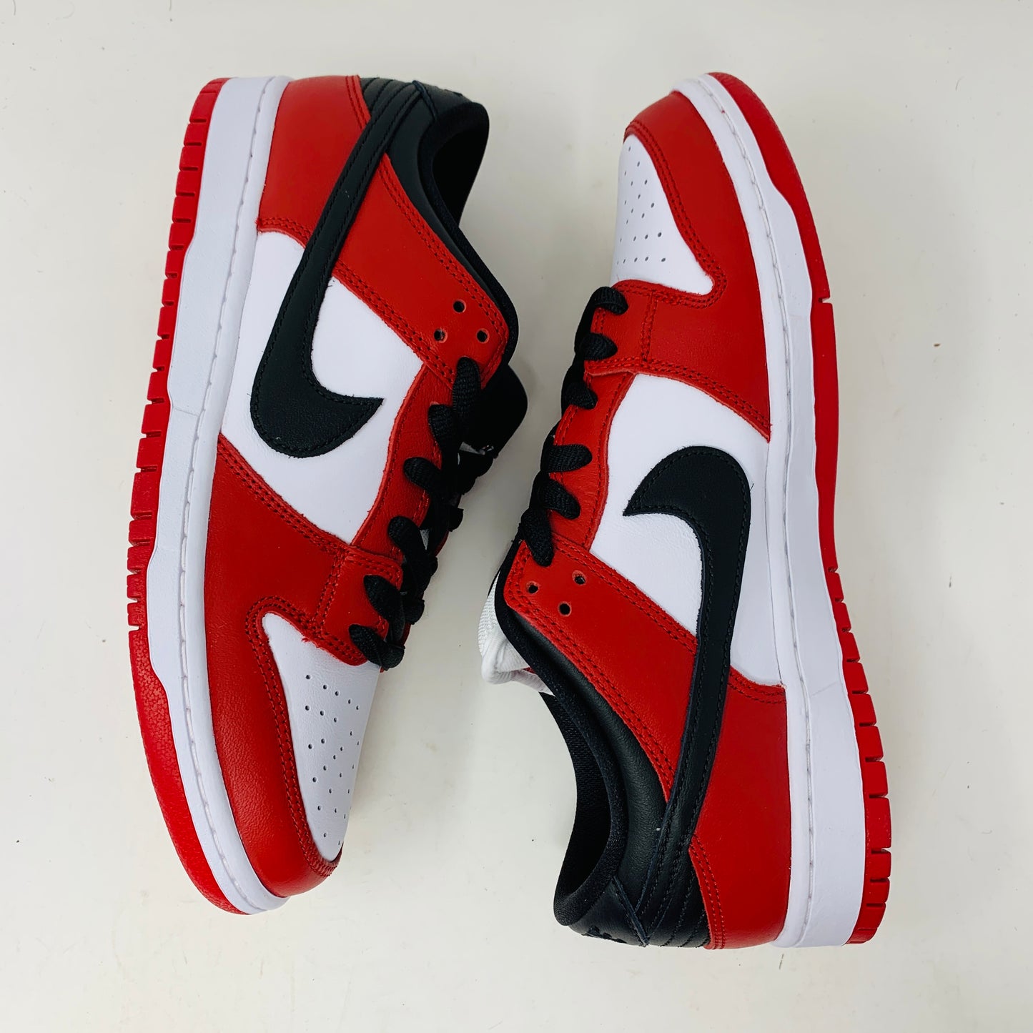 A brand new Nike SB Dunk Low J-Pack Chicago sneaker in red, white, and black sits on a purple Nike SB box with extra white laces, highlighted by a black swoosh and guaranteed 100% authentic.