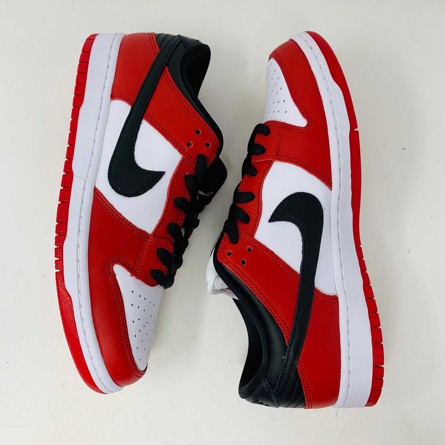 A brand new Nike SB Dunk Low J-Pack Chicago sneaker in red, white, and black sits on a purple Nike SB box with extra white laces, highlighted by a black swoosh and guaranteed 100% authentic.