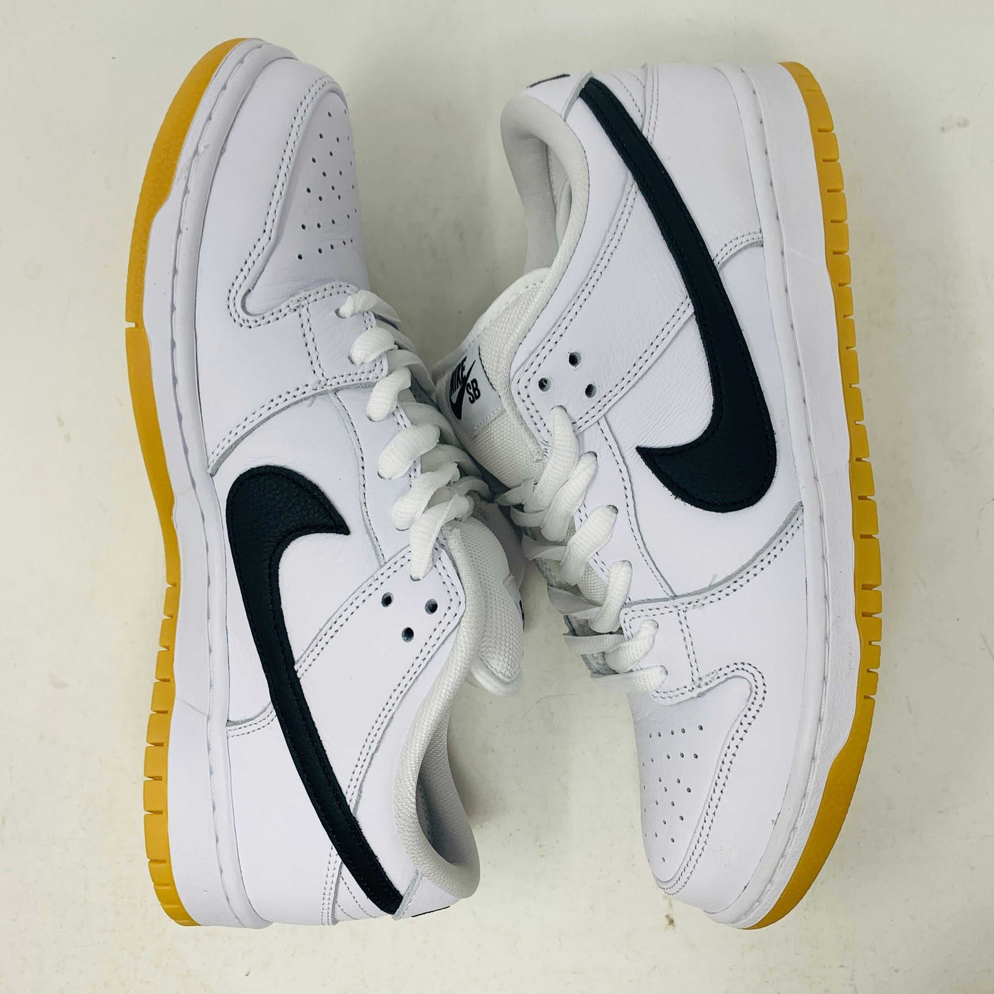 A brand new Nike SB Dunk Low in white with a black swoosh, white laces, and a gum sole rests on a 2023 purple Nike SB shoebox featuring bold white text. The profile view showcases its authentic design.