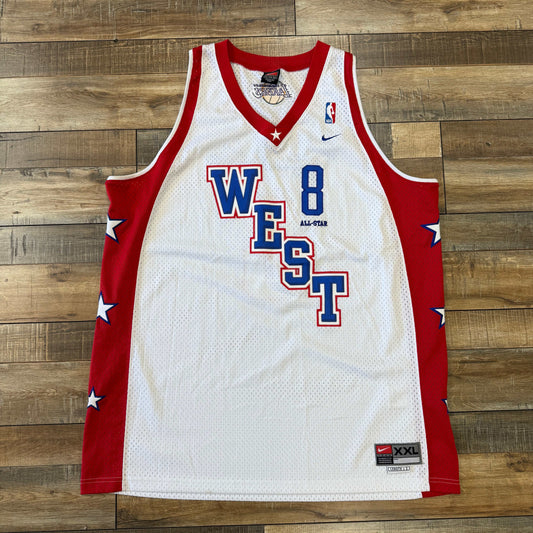 The 2004 Kobe All Star Jersey by Nike is a preowned XXL white and red basketball jersey featuring WEST and the number 8. Blue stars adorn the sides along with All-Star branding. Displayed on a wooden floor, it exudes unique charm.