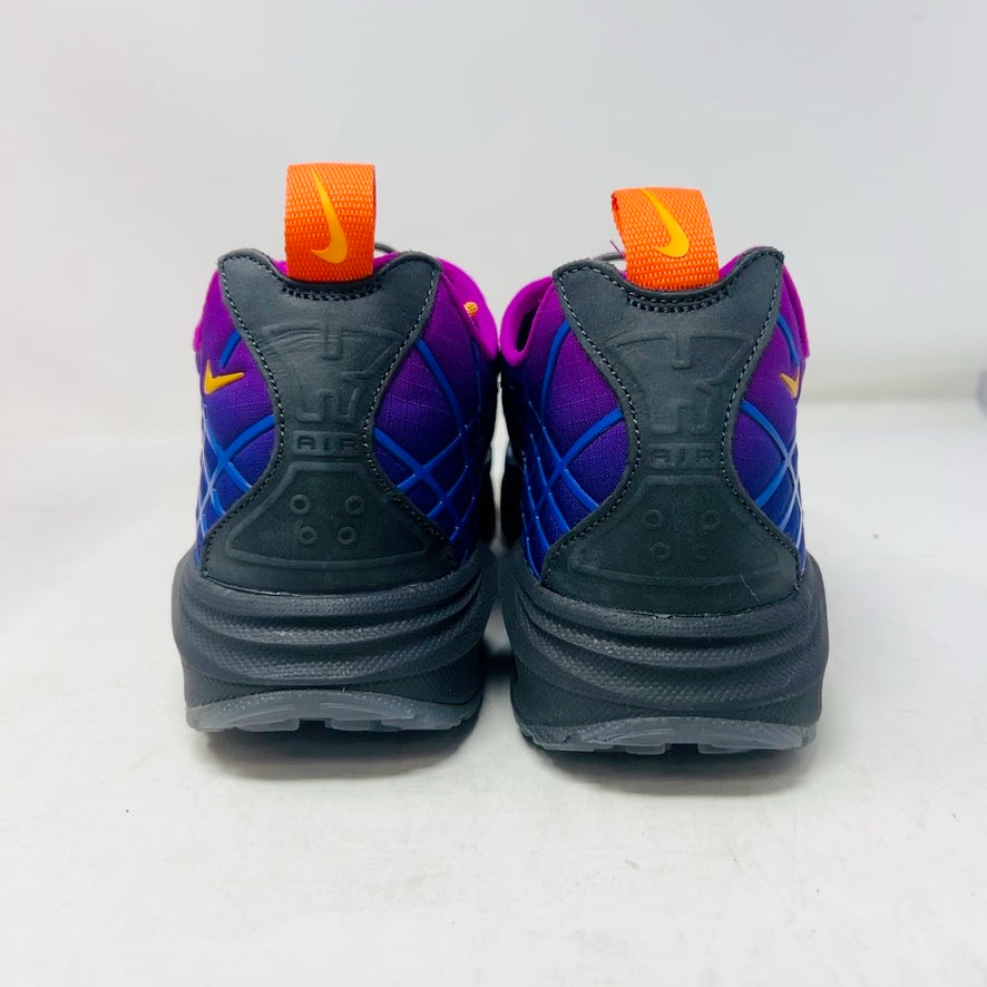 Displayed on an orange Nike shoe box is the colorful Nike Air Max Sunder SP Kids of Immigrants Sun Down sneaker, featuring a grid pattern with shades of purple, blue, and gray, complemented by orange accents and a swoosh logo. The shoe box shows a k-i logo inside a circle.
