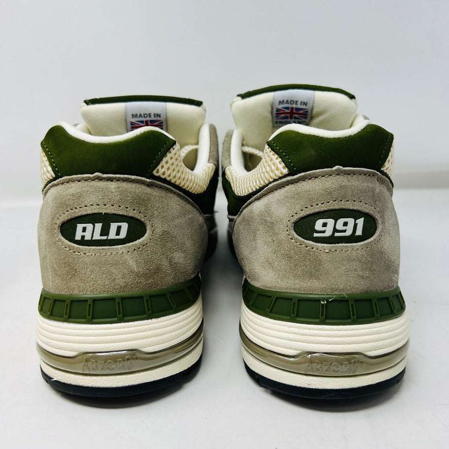 A pair of Holy Grounds New Balance 991 Aime Leon Dore MiUK Grey sneakers in gray, green, and beige are displayed on their shoebox. Comes with extra green and gray laces. The 2022 box details the size and model.