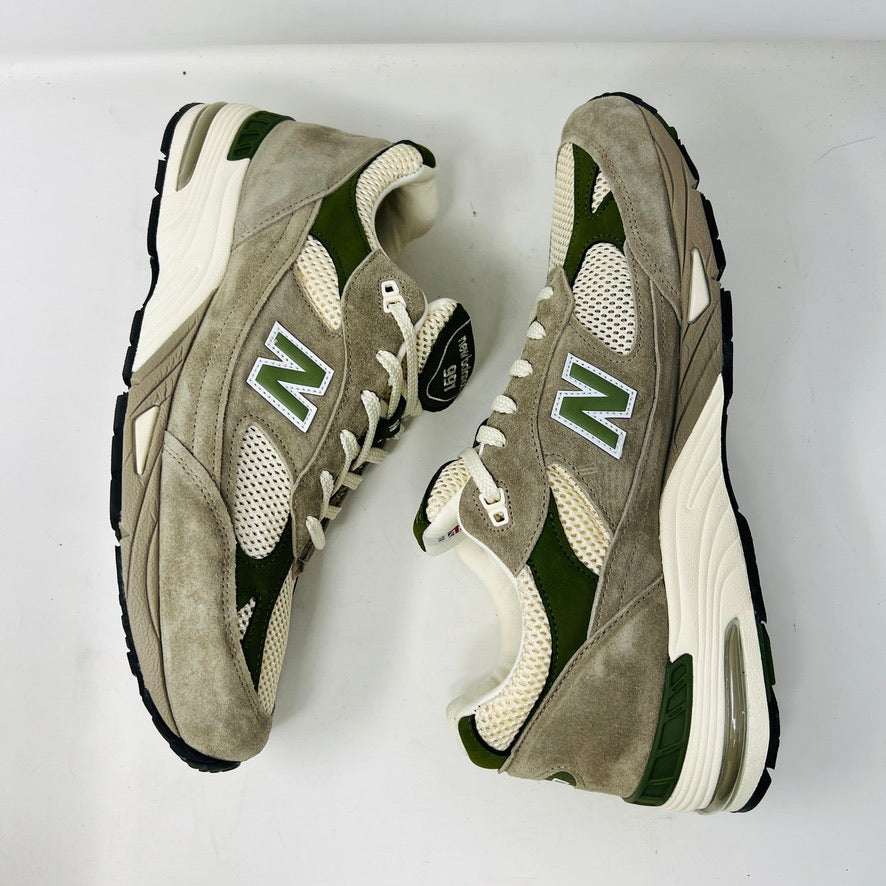 A pair of Holy Grounds New Balance 991 Aime Leon Dore MiUK Grey sneakers in gray, green, and beige are displayed on their shoebox. Comes with extra green and gray laces. The 2022 box details the size and model.