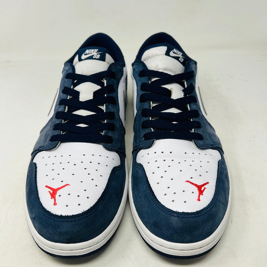 The Jordan 1 Low SB Midnight Navy sneakers, with white and navy panels and a side Nike swoosh, are displayed on a pristine shoebox. A spare set of white laces featuring the Nike SB logo in Metallic Silver is also included.