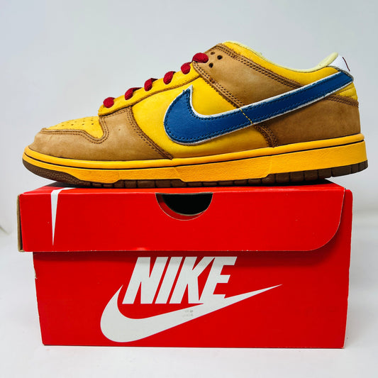 Nike SB Dunk Low Newcastle Brown Ale sneaker with yellow and brown design, displayed on red Nike box.