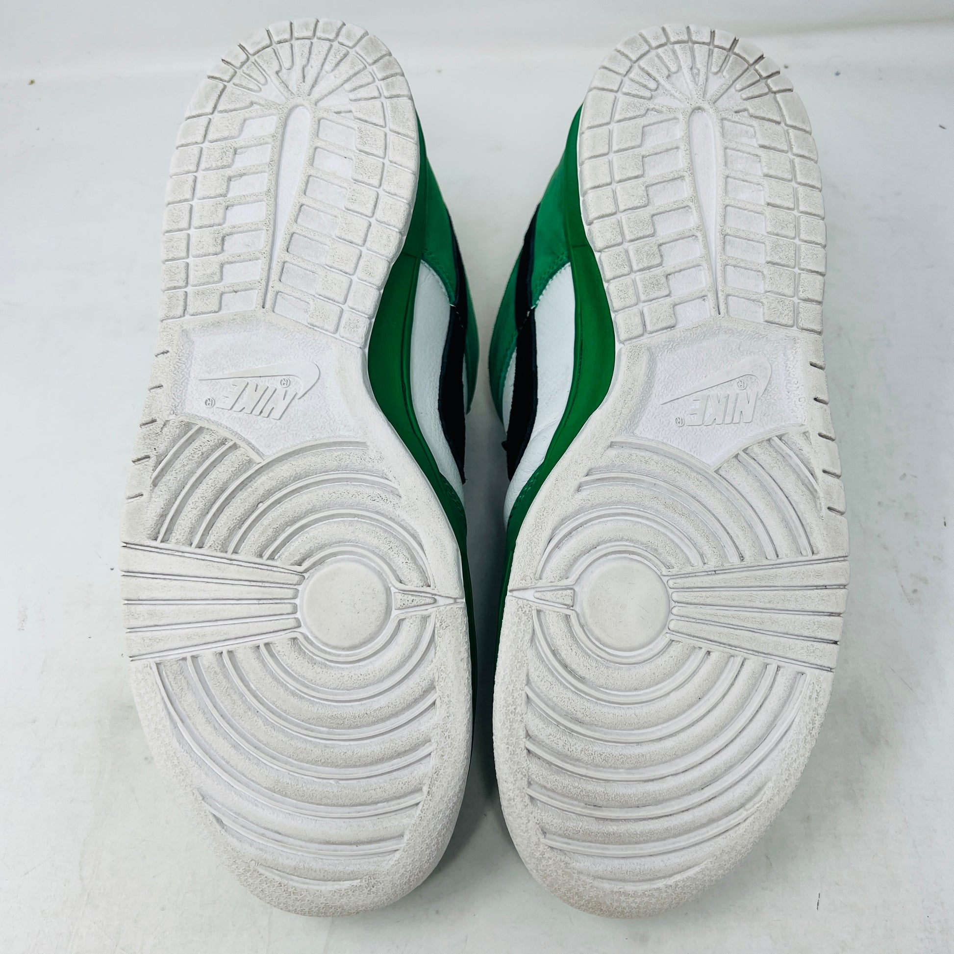 The Nike SB Dunk Low Heineken sneaker, featuring a green, white, and black design with red laces and a red star on the heel, sits on its box. A small package of green shoelaces is beside it. The box displays the size and Nike branding.