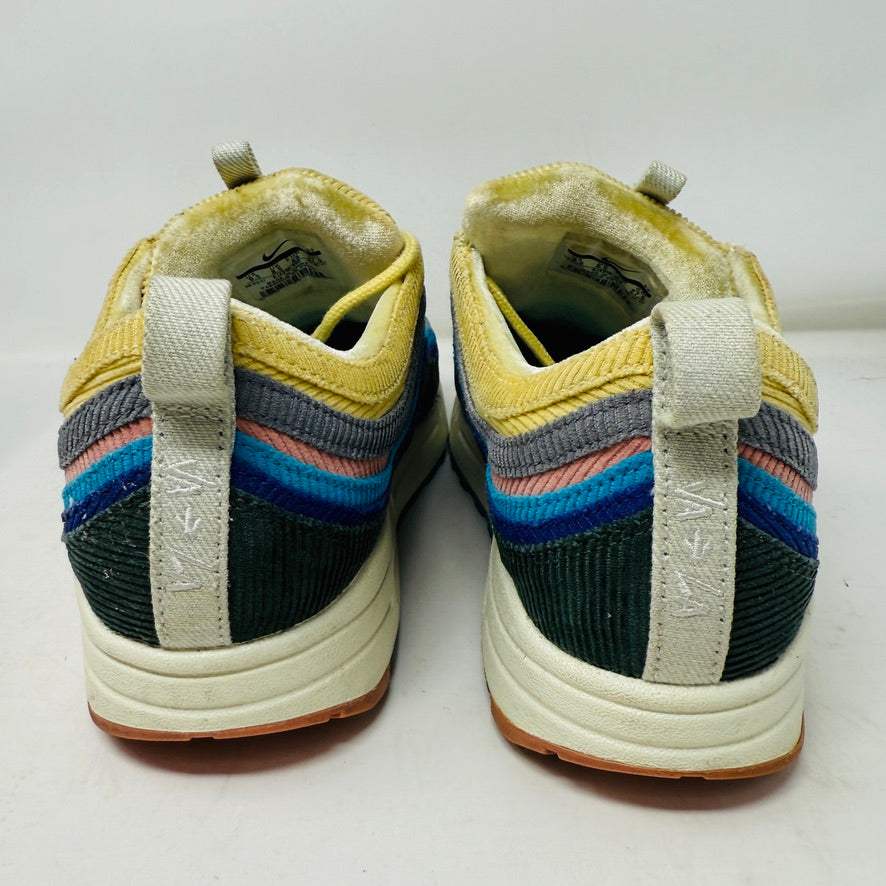 The Nike Air Max 1/97 Sean Wotherspoon sneaker, featuring a multicolored wave-like design, rests on a New Balance box and includes extra blue, white, and dark blue laces. It showcases an authentic air cushion in the sole.