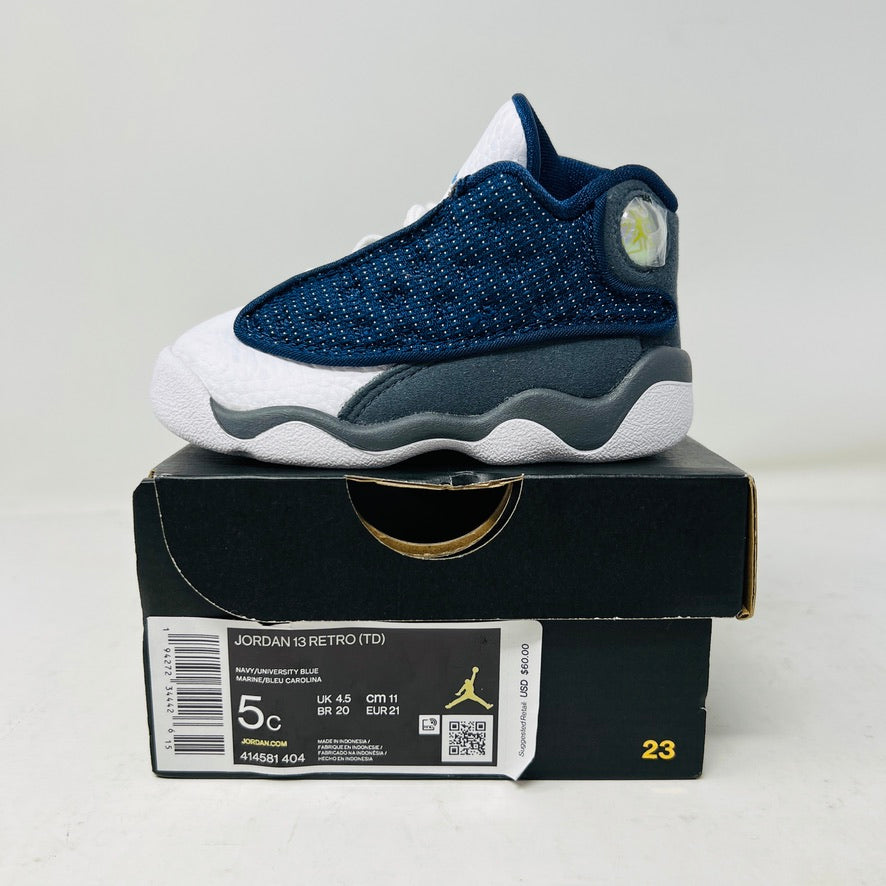 The Jordan 13 Retro Flint (2020) (TD) by Jordan, in a striking blue and white color with textured sides and a holographic heel, is showcased on its pristine box displaying size and style info.