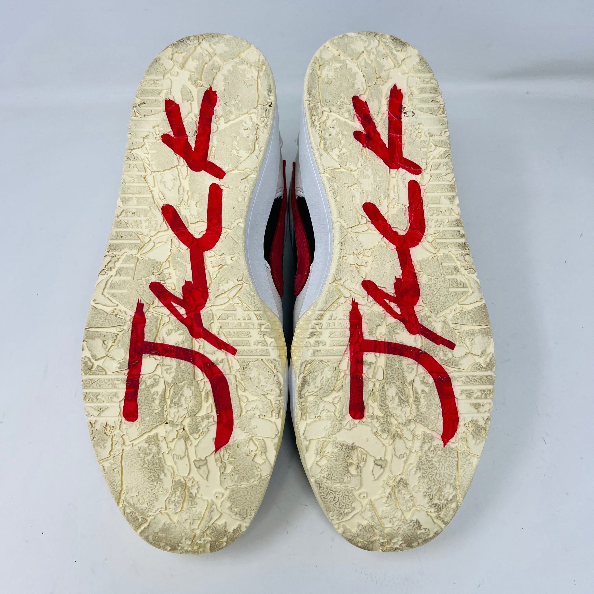 The Jordan Jumpman Jack TR Travis Scott University Red sneakers, black and white with red swooshes, rest on a brown shoe box. Three lace sets in red, cream, and black with white speckles are individually packaged in front. The box label displays sizes 9 and 10.5.