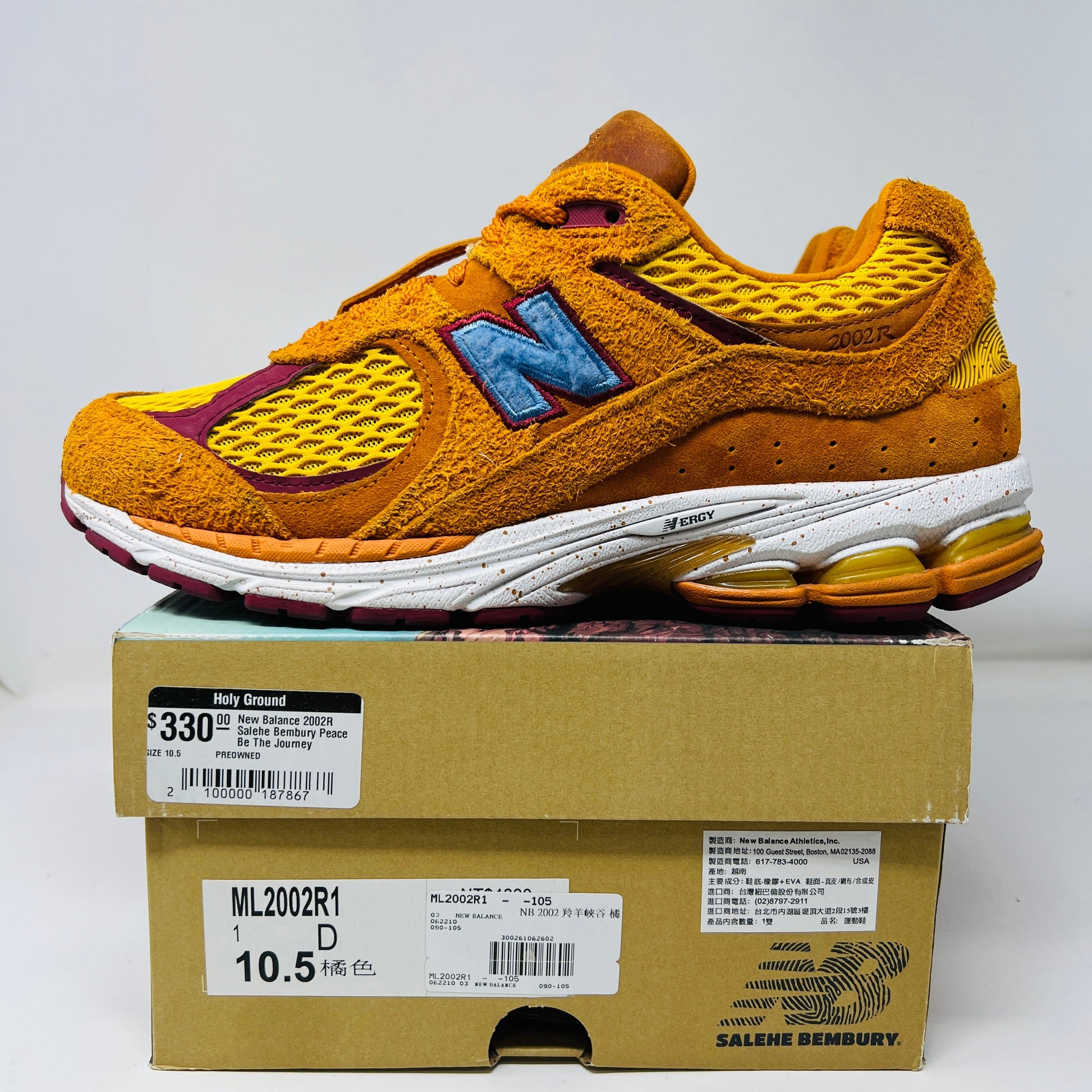A New Balance 2002R Salehe Bembury Peace Be The Journey sneaker in vibrant orange and yellow with a blue N logo is displayed on a shoebox. It features textured design, visible sole cushioning, and extra laces. Tagged as model ML2002R1, size 10.5, priced at $330.