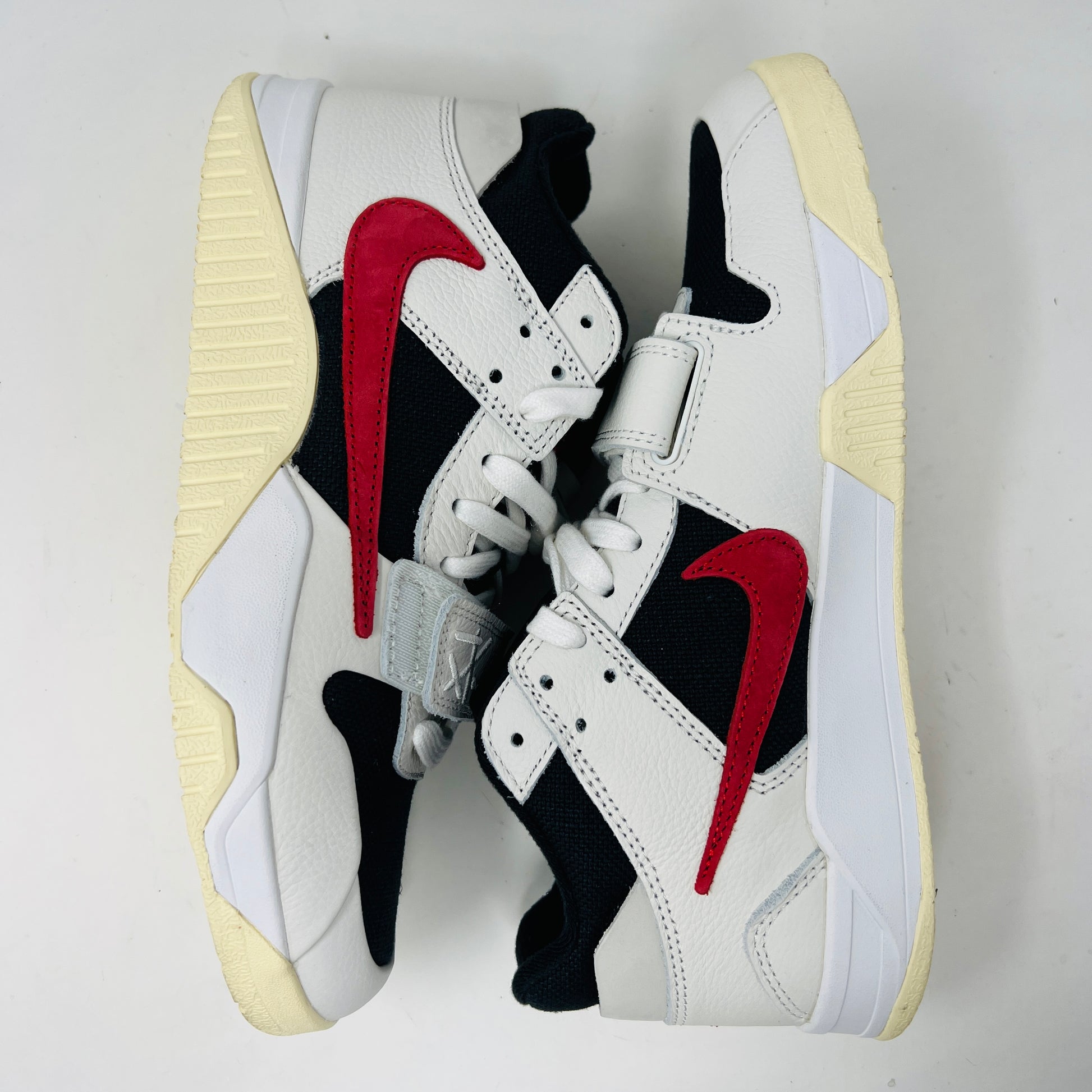 The Jordan Jumpman Jack TR Travis Scott University Red sneakers, black and white with red swooshes, rest on a brown shoe box. Three lace sets in red, cream, and black with white speckles are individually packaged in front. The box label displays sizes 9 and 10.5.