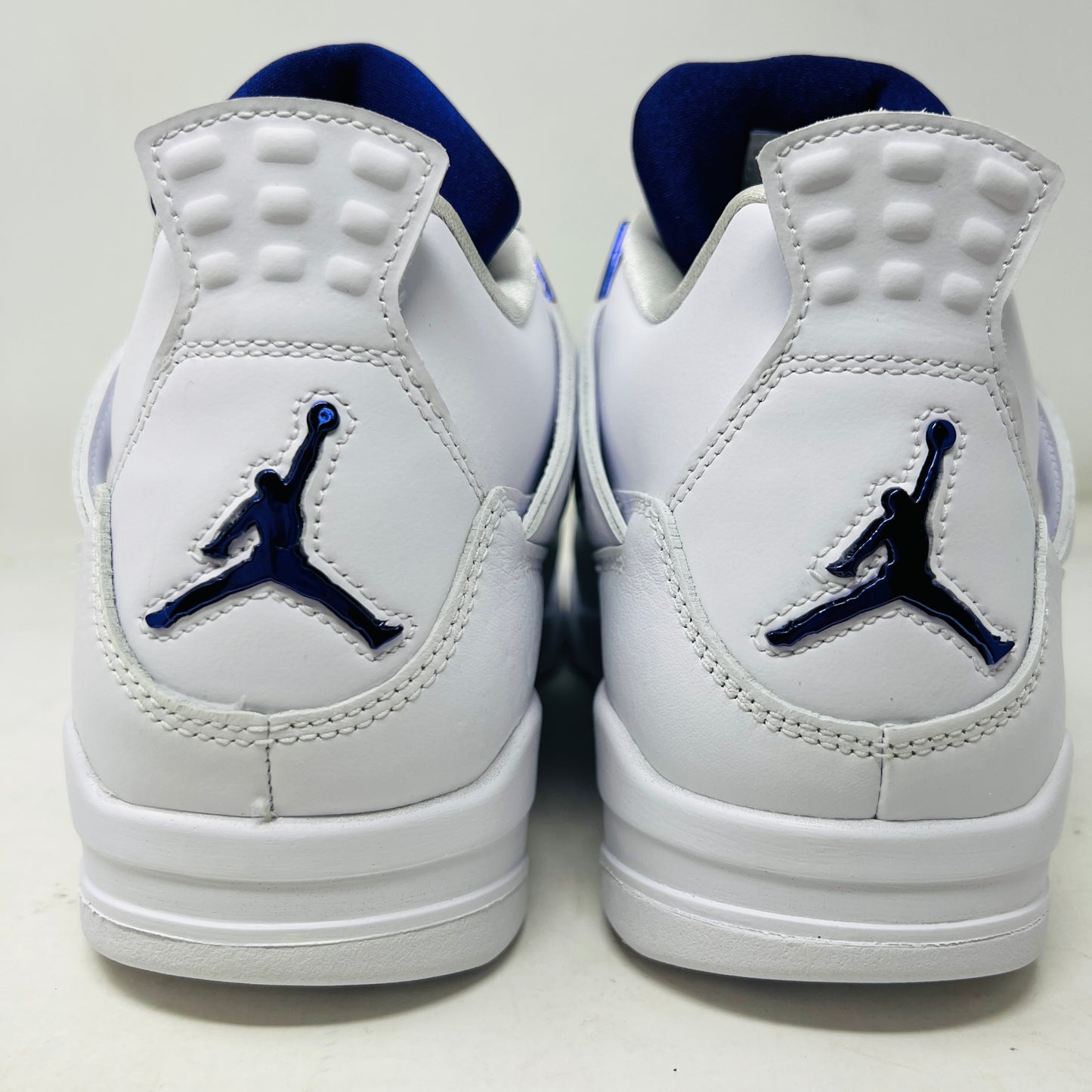 The Jordan 4 Retro Metallic Purple sneaker features white material with blue mesh accents, a visible air cushion in the heel, textured sole, angular overlays, and a padded collar. Note: no box included.
