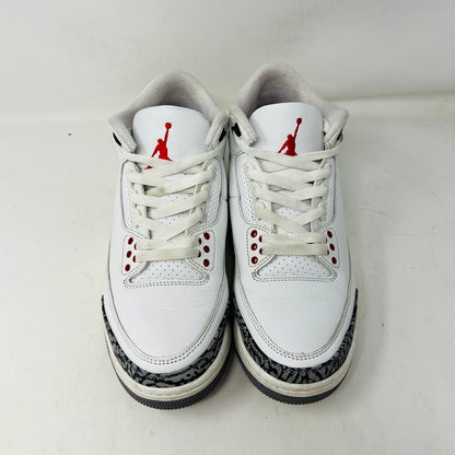 The Jordan 3 Retro White Cement Reimagined sneakers by Jordan feature a clean white upper with red accents, gray and black patterned trim on the toe and heel, white laces, and a red logo on the tongue, displayed upright on a pristine white background—perfect for everyday wear.