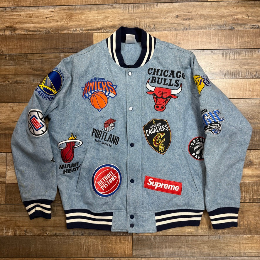 The preowned Supreme Nike/NBA Teams Warm-Up Jacket Denim features a gray design with a black collar and cuffs, adorned with embroidered NBA team logos, including the Bulls, Knicks, Heat, and more. It also sports a red Supreme patch on the front.