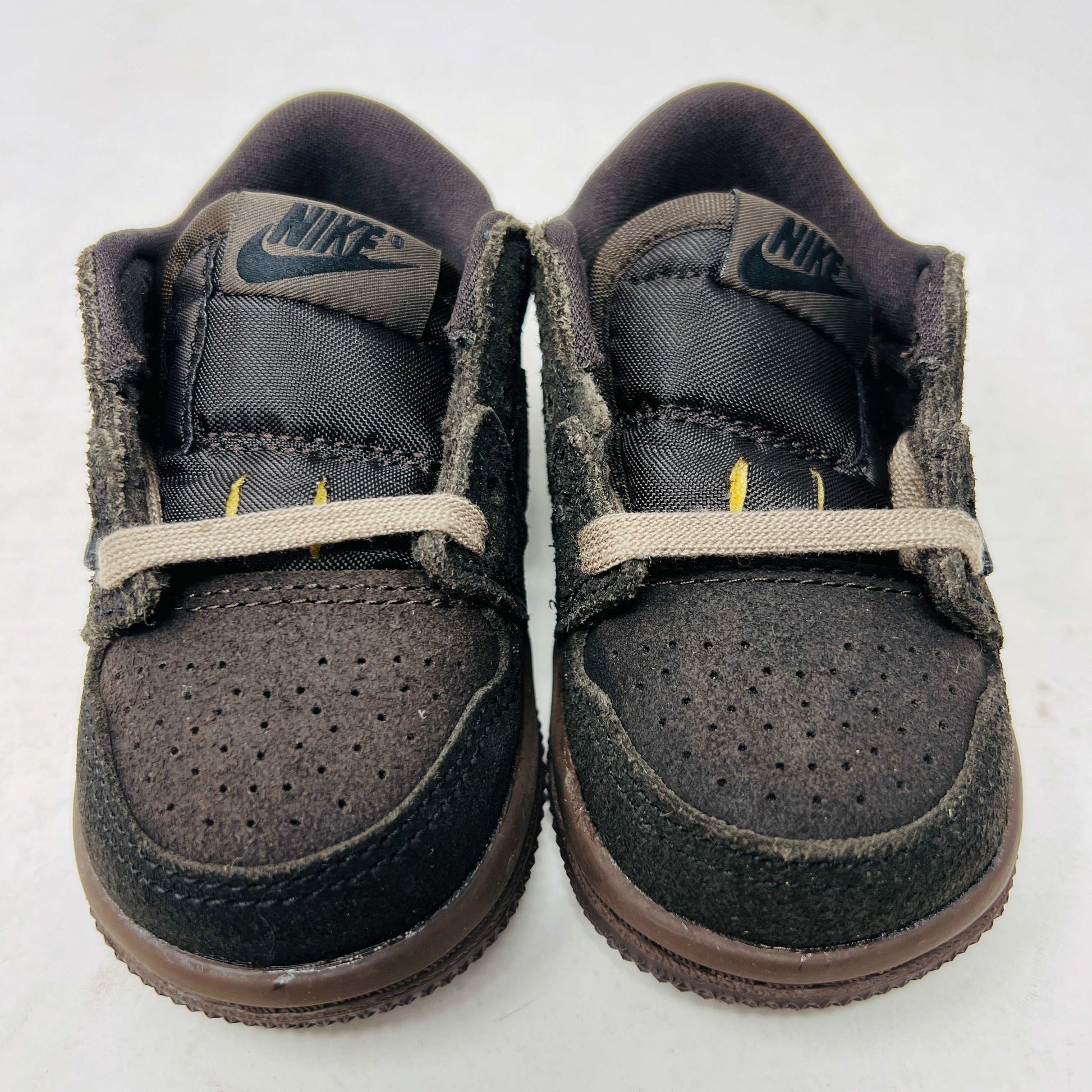 A Jordan 1 Retro Low OG SP Travis Scott Velvet Brown (TD) sneaker with a unique swoosh design sits on a white shoebox. It includes extra pink and black laces, is 100% authentic, brand new, and ready to elevate your style with its sleek look.