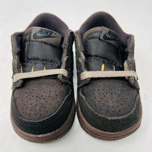 A Jordan 1 Retro Low OG SP Travis Scott Velvet Brown (TD) sneaker with a unique swoosh design sits on a white shoebox. It includes extra pink and black laces, is 100% authentic, brand new, and ready to elevate your style with its sleek look.